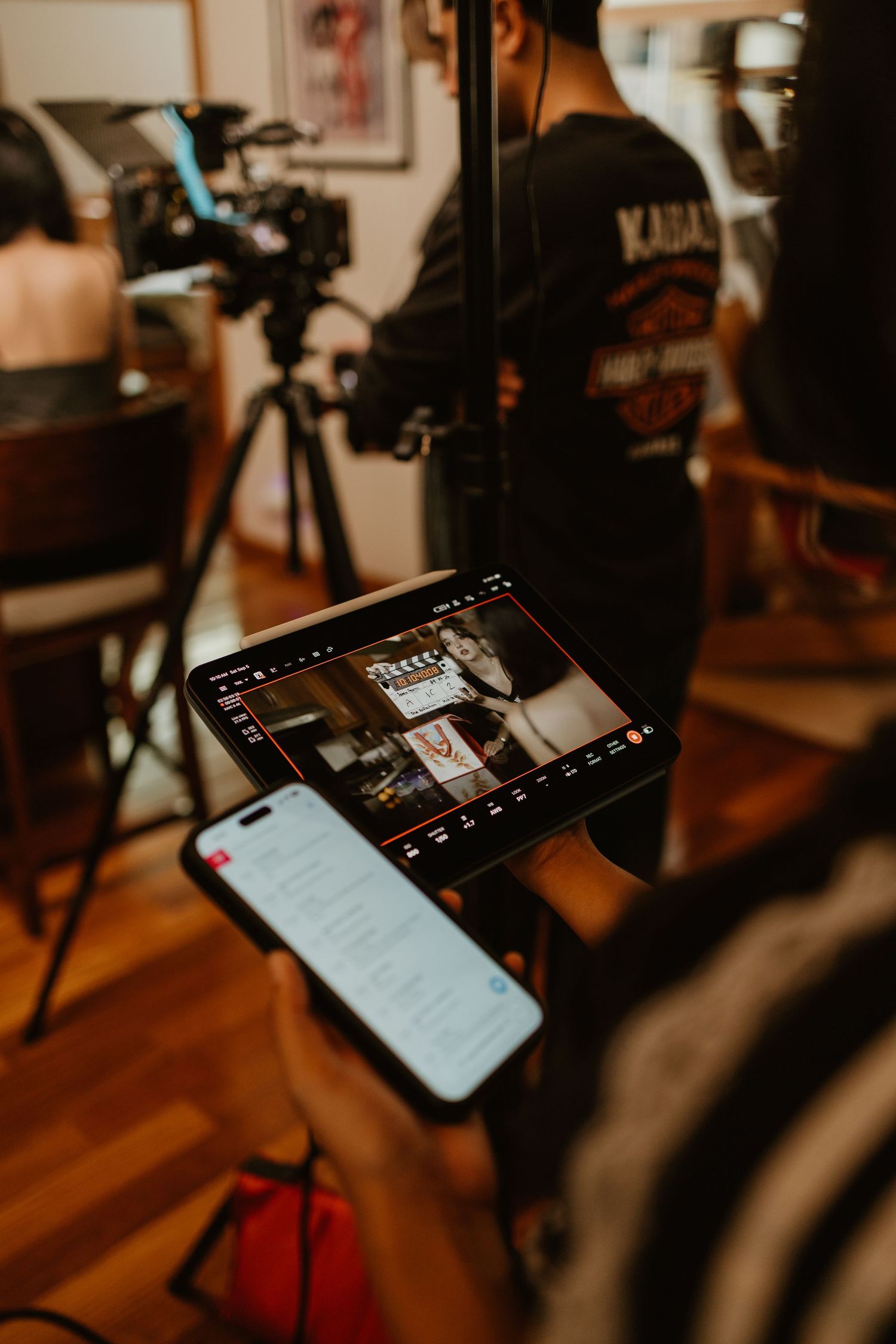 Behind-the-scenes video production with tablet monitor, smartphone, and camera on tripod in indoor studio.