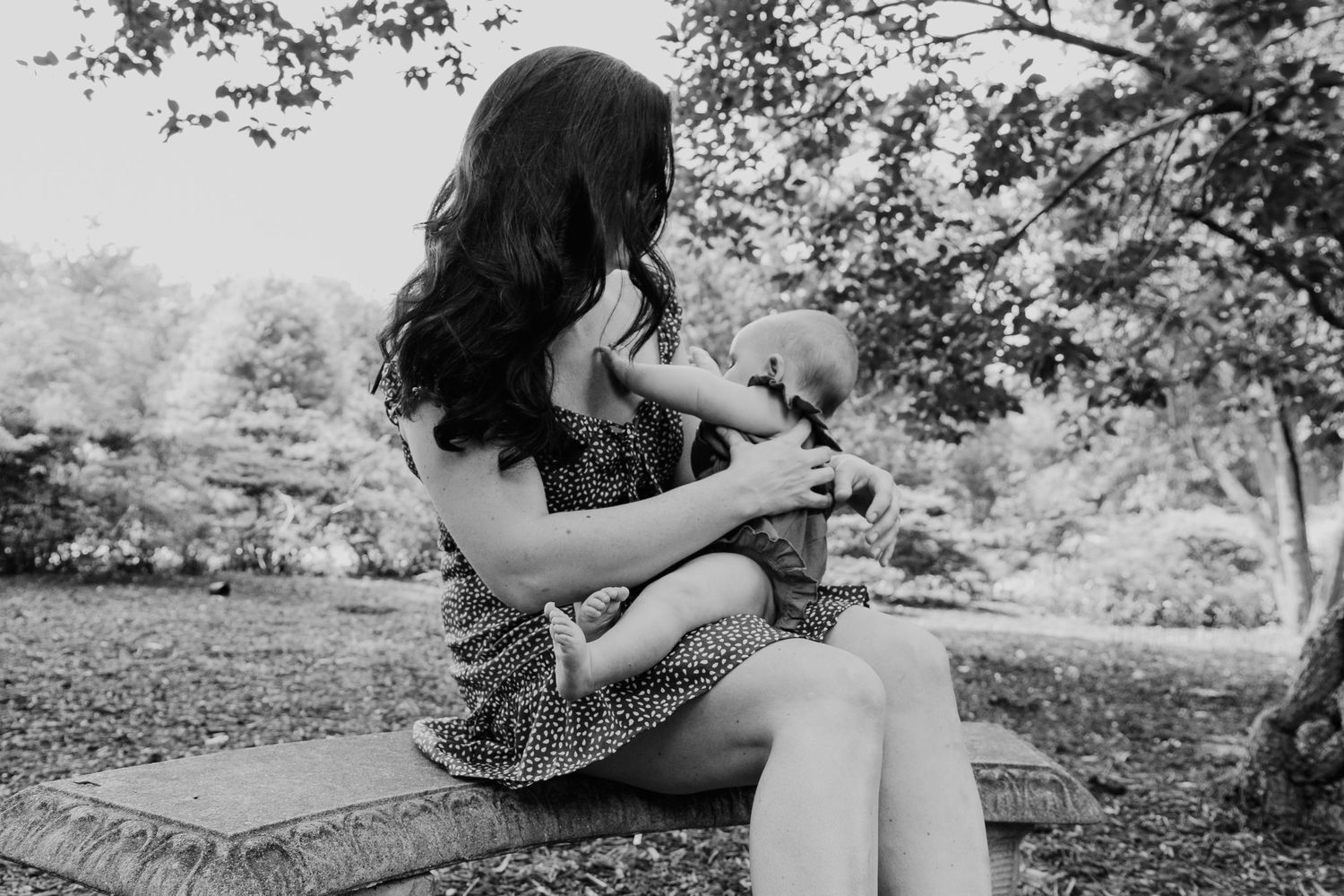 Black and white photo of woman sitting on bench holding small dog in park.