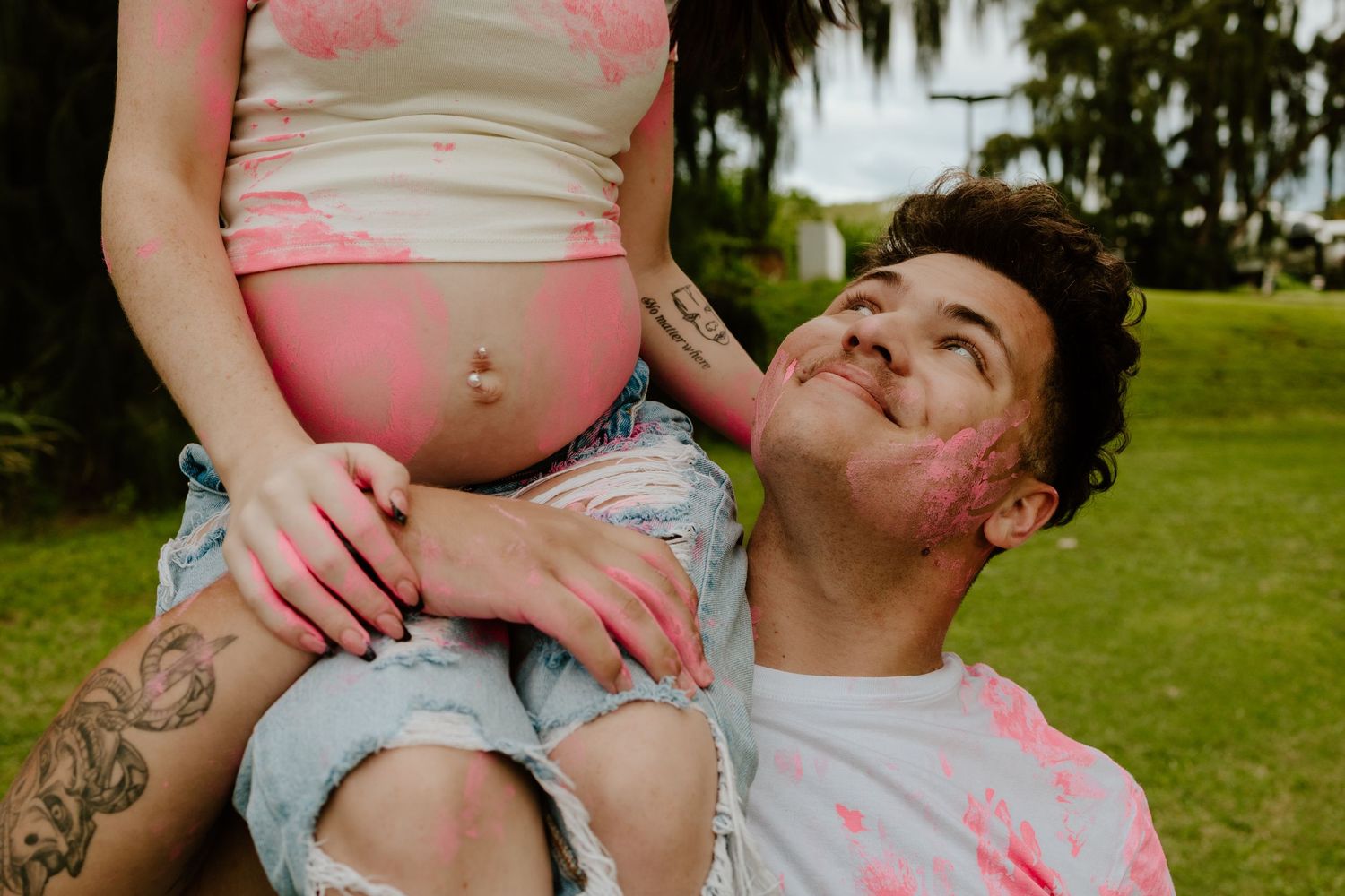 Couple celebrating girl gender reveal with pink paint, man looking up at pregnant partner.