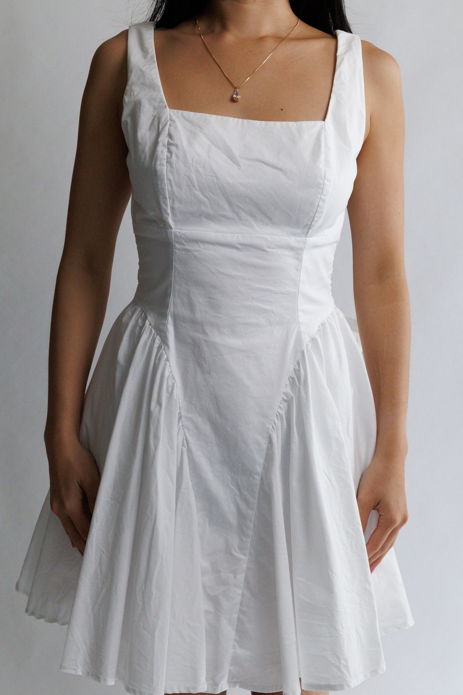 Woman wearing a white sleeveless fit-and-flare mini dress with square neckline and structured bodice.