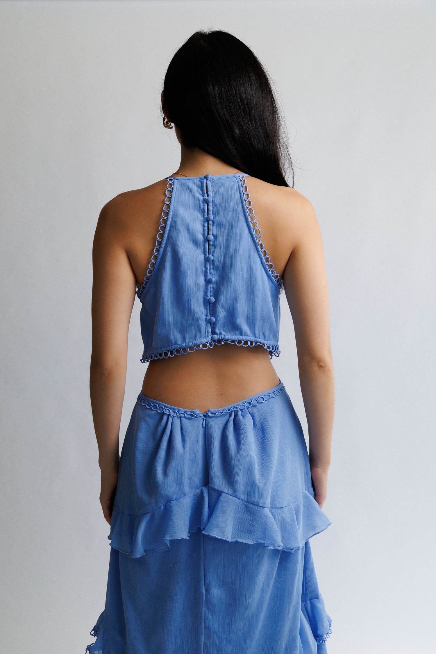 Back view of woman wearing blue halter crop top with lace trim and matching ruffled tiered maxi skirt.