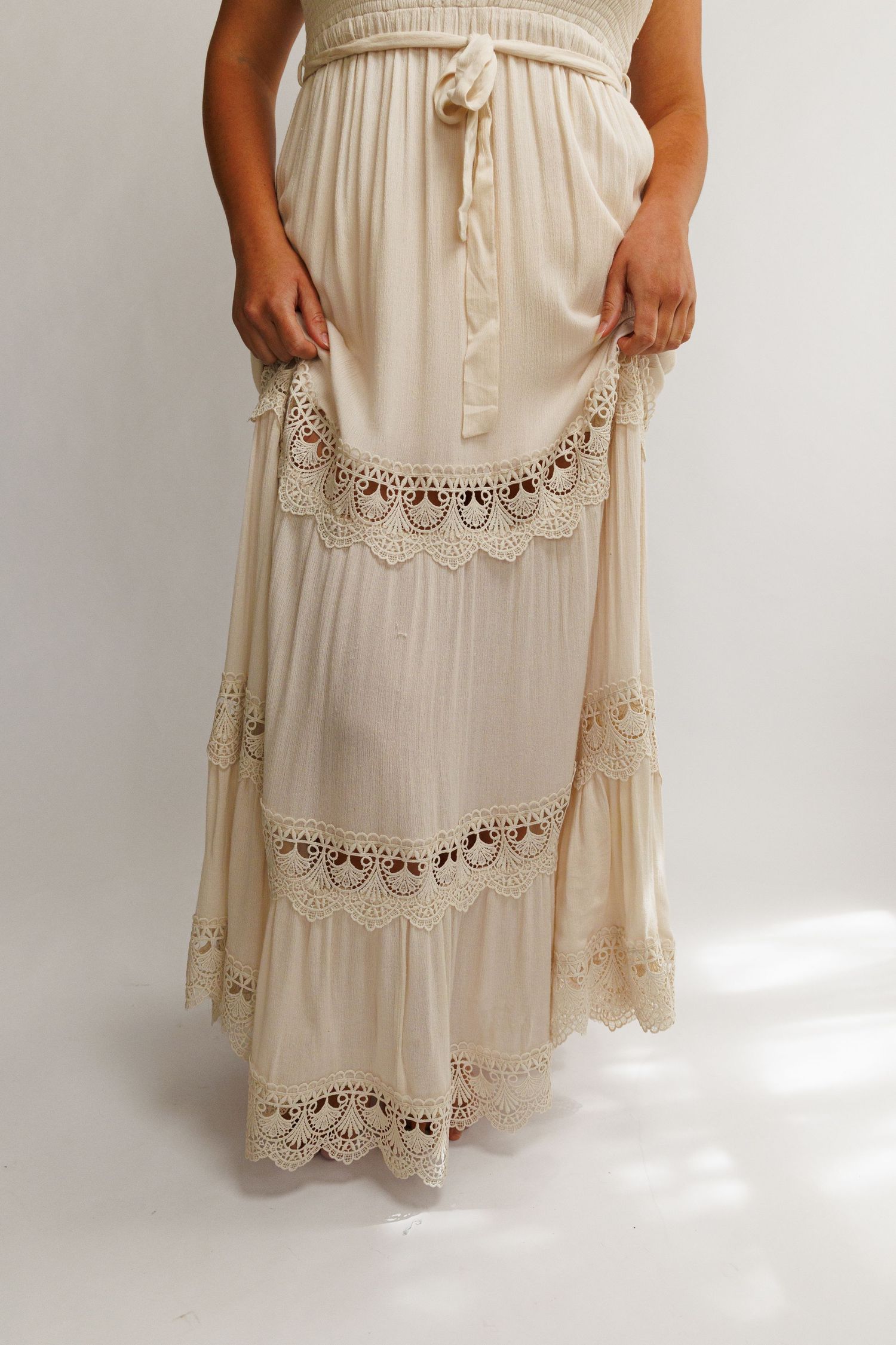 Cream boho maxi skirt with crochet lace trim details and tiered layers, featuring a drawstring waist.