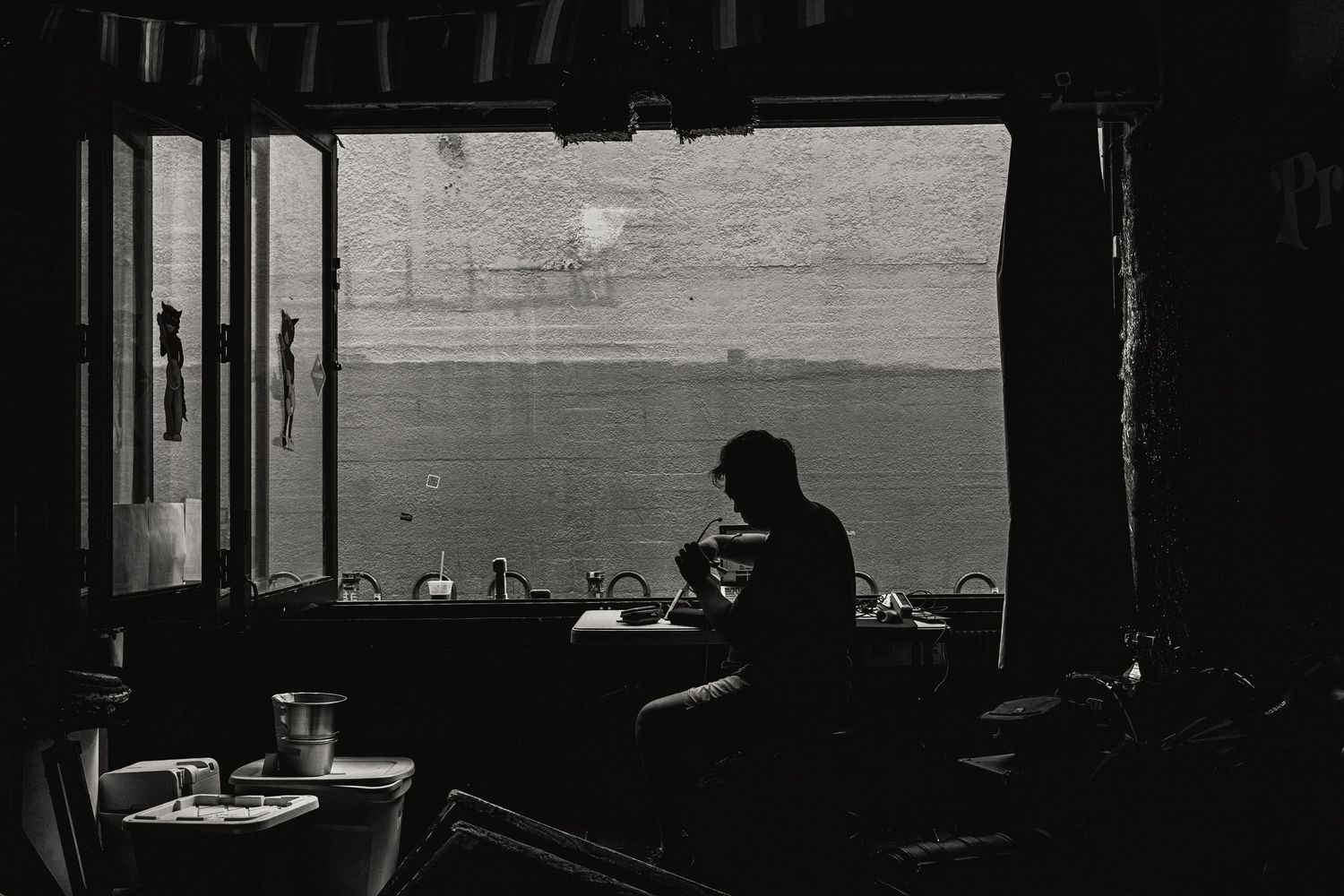 Silhouetted person sitting alone by a large window in a dimly lit diner, black and white photography.