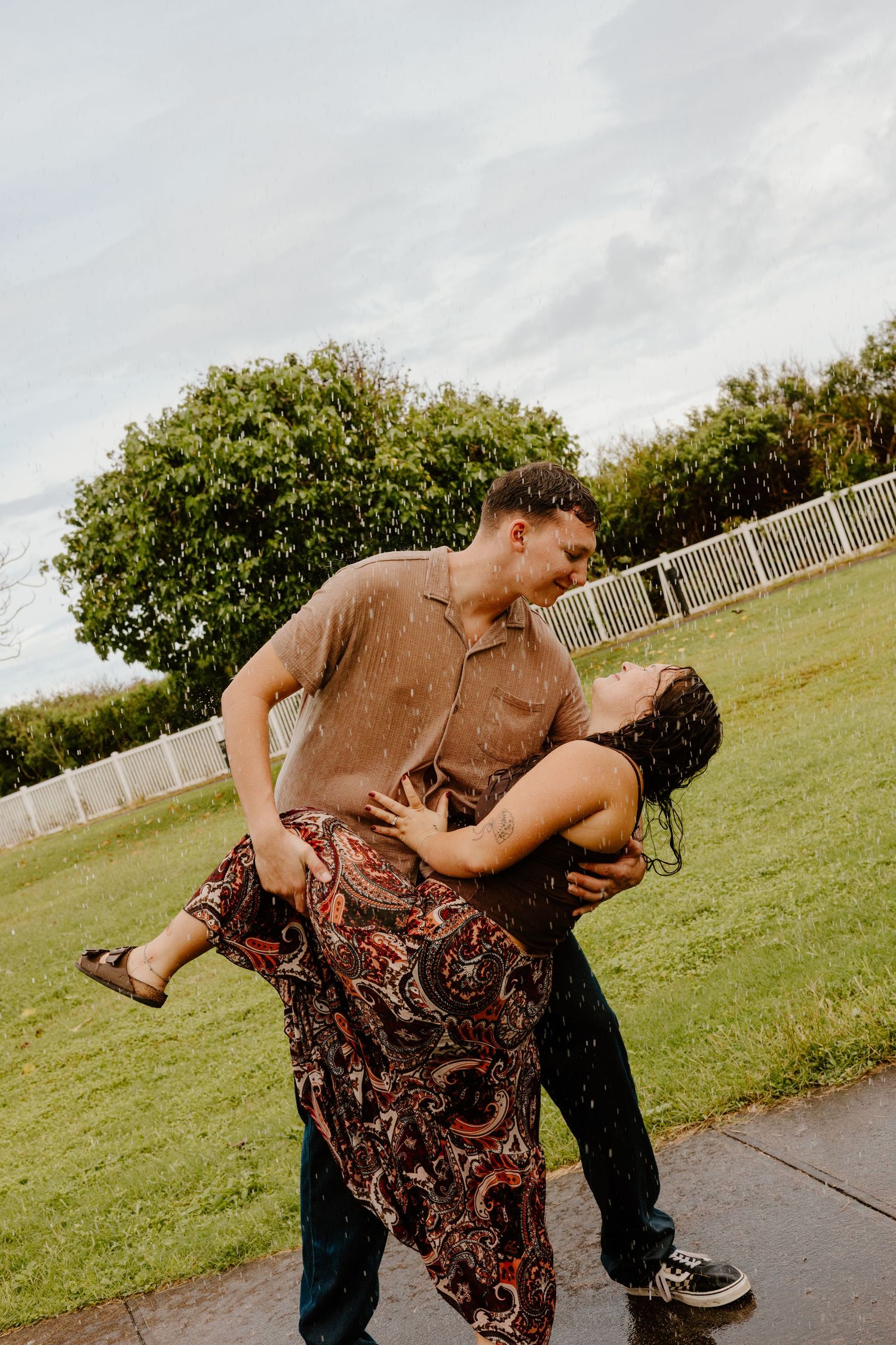 Couple sharing a romantic dip kiss in the rain on a green lawn.