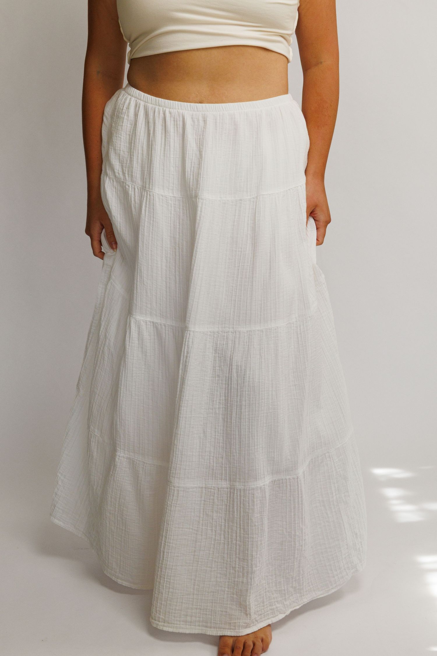 White tiered maxi skirt with elastic waist in lightweight gauze fabric, paired with a cream crop top.