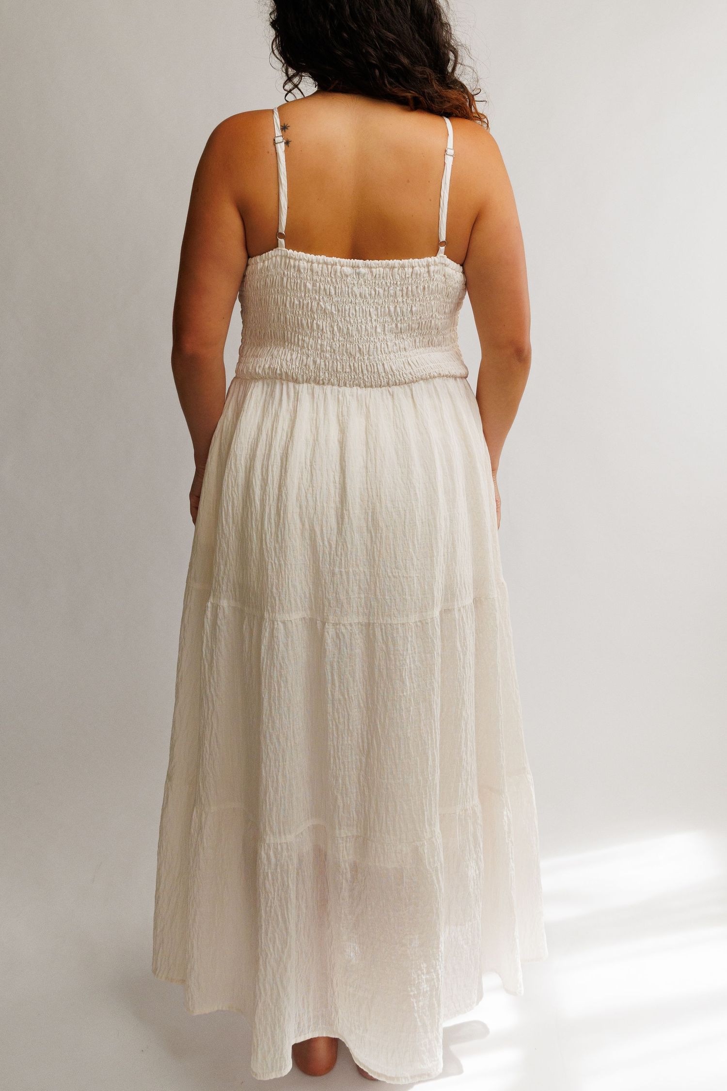 Back view of a woman wearing a white smocked bodice maxi dress with tiered skirt and spaghetti straps.