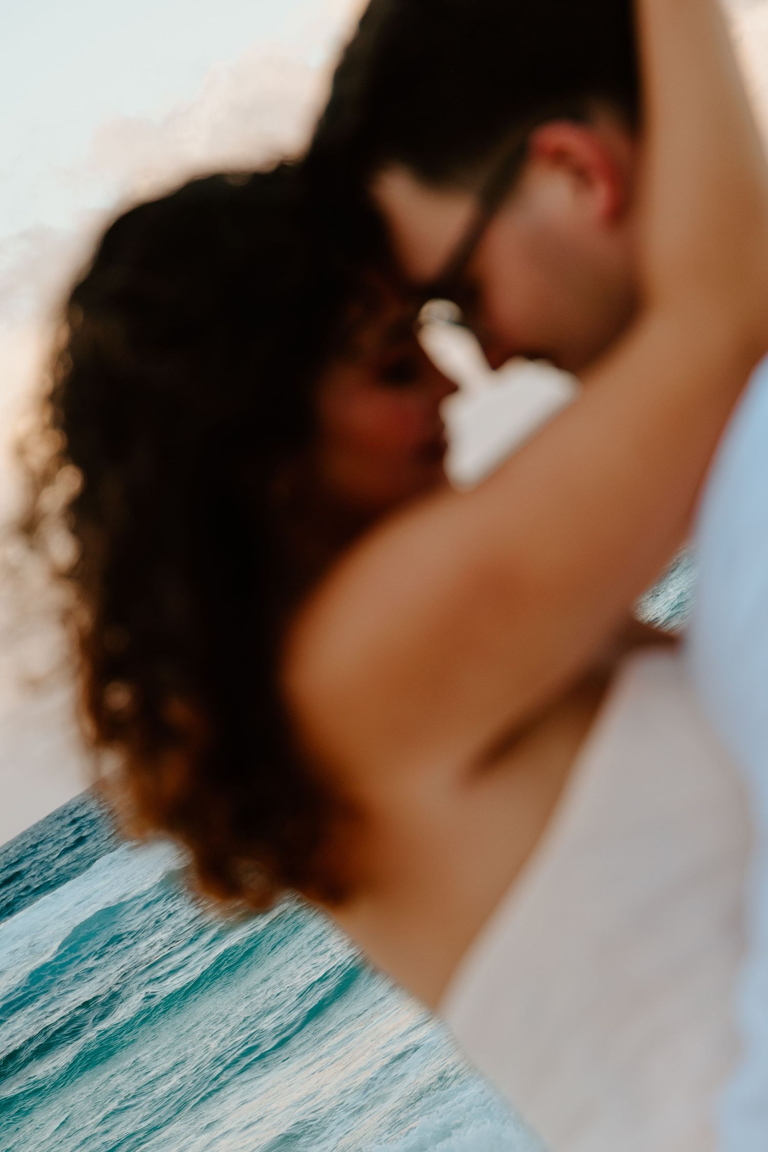A blurred romantic couple sharing an intimate moment near the ocean waves at sunset on a beach.