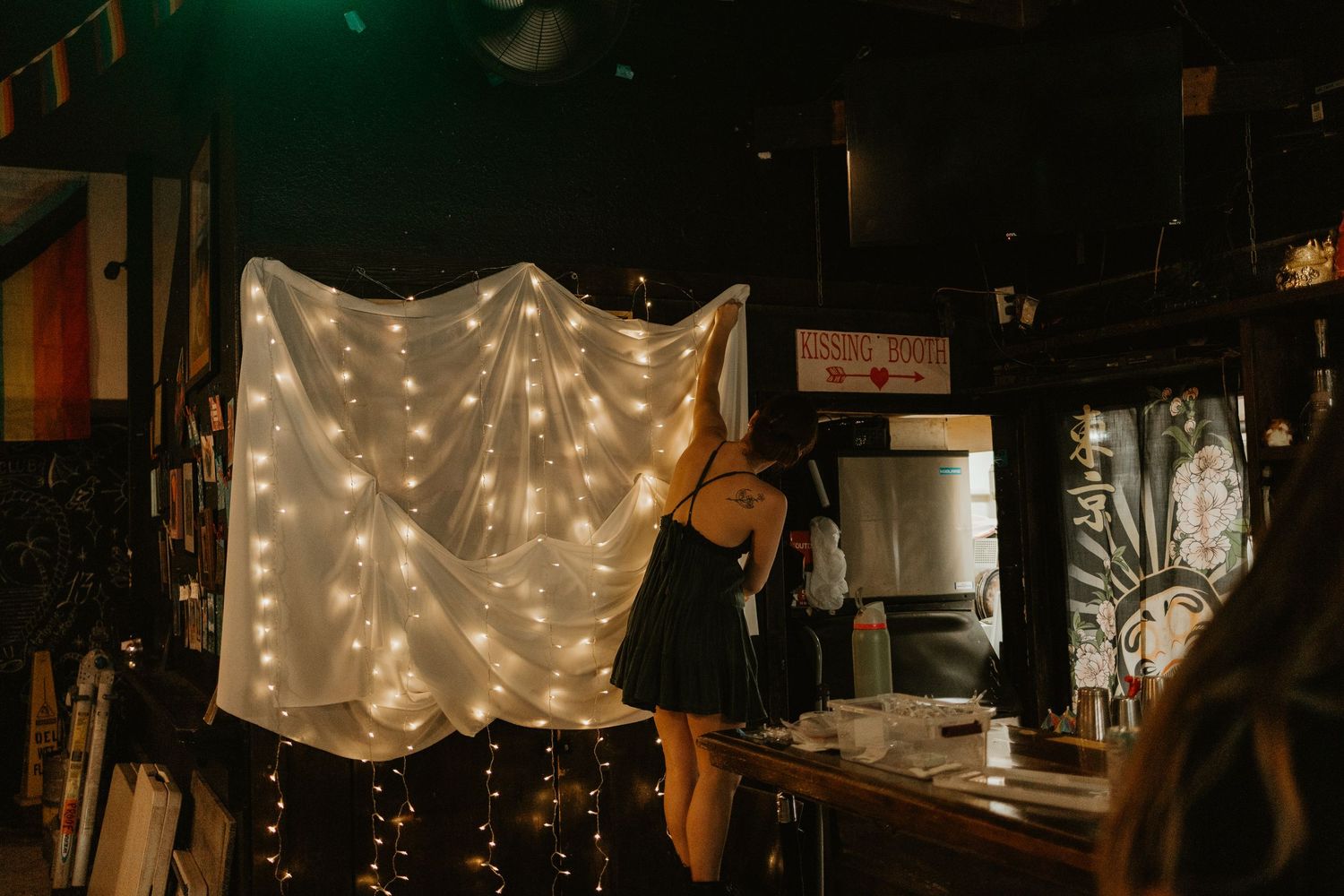 Woman holding a glowing fairy light curtain in a dimly lit bar or venue setting.