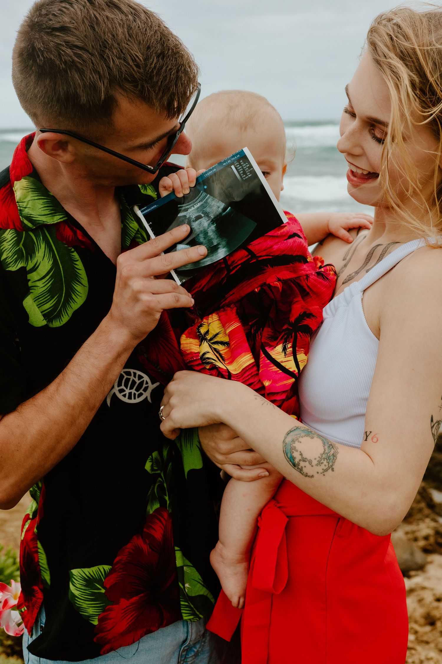 Happy couple holding baby and ultrasound photo during beach maternity announcement session.