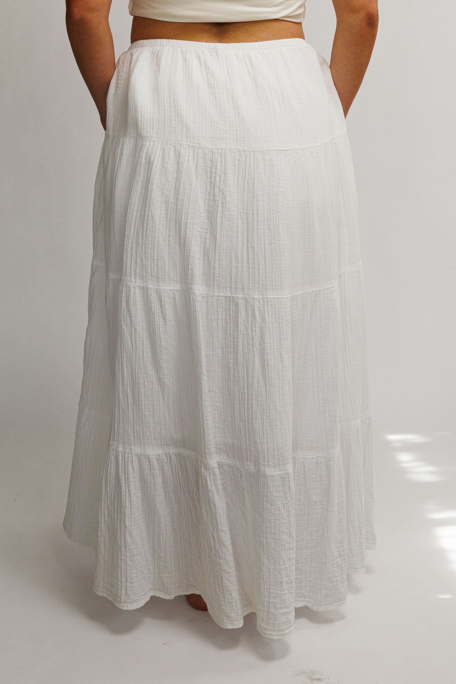White tiered maxi skirt in textured cotton fabric with elastic waistband, shown from the back on a model.