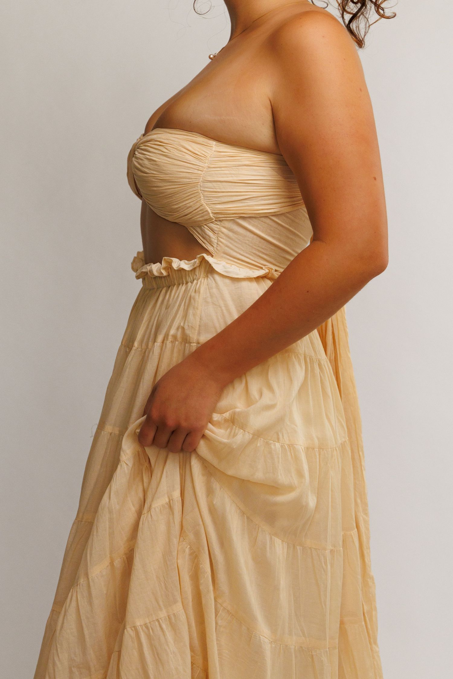 Woman wearing a strapless ruched bandeau top and tiered maxi skirt set in soft golden yellow fabric.