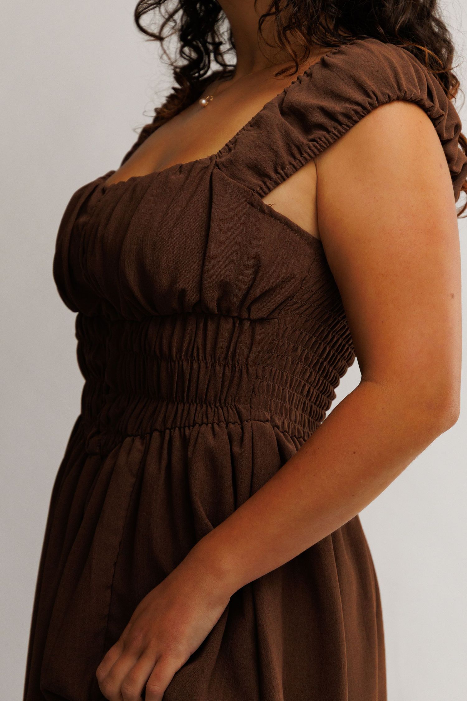 Close-up of a brown smocked waist midi dress with ruffle cap sleeves on a model.