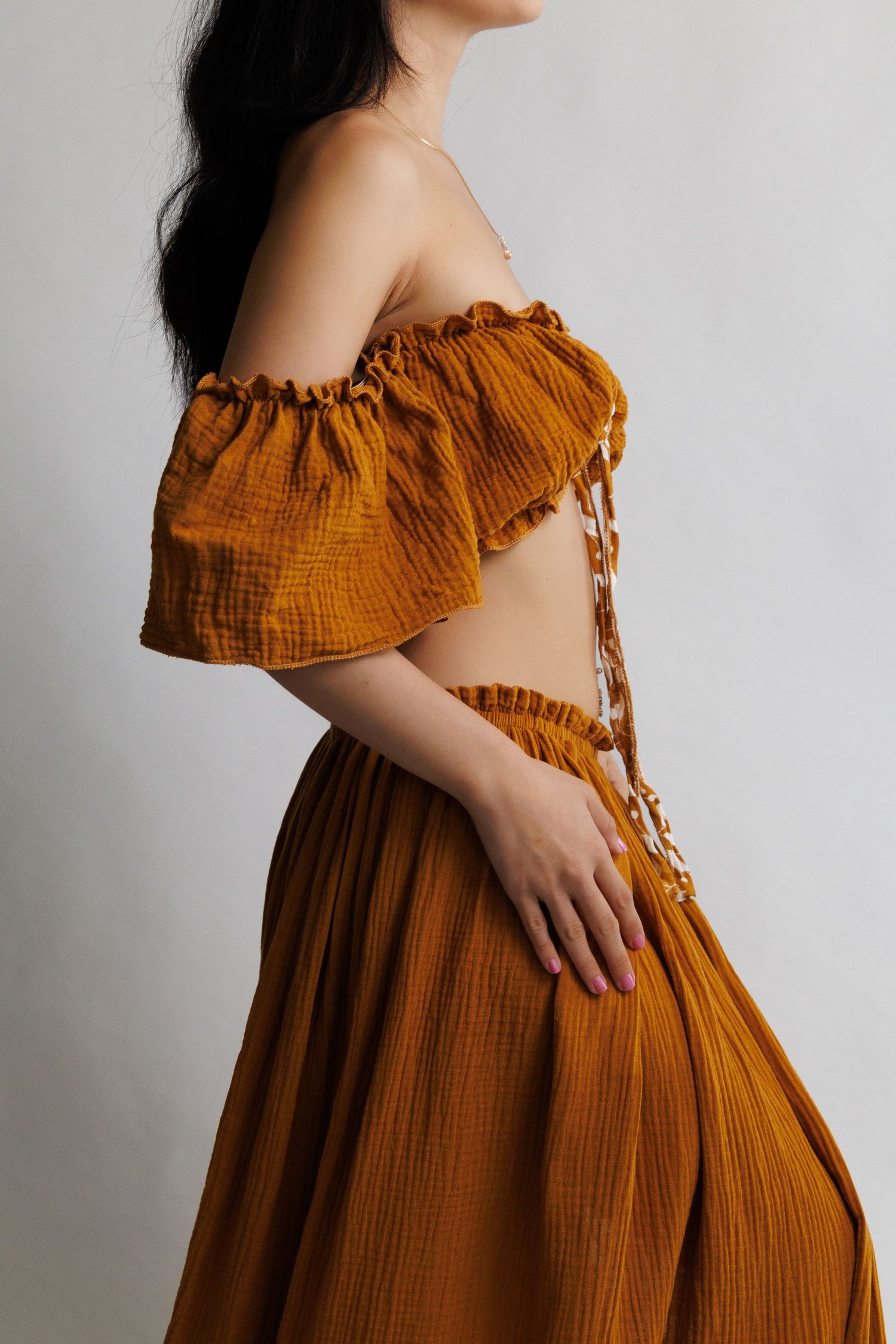 Woman wearing a rust orange off-shoulder crop top and matching maxi skirt set in textured cotton fabric.