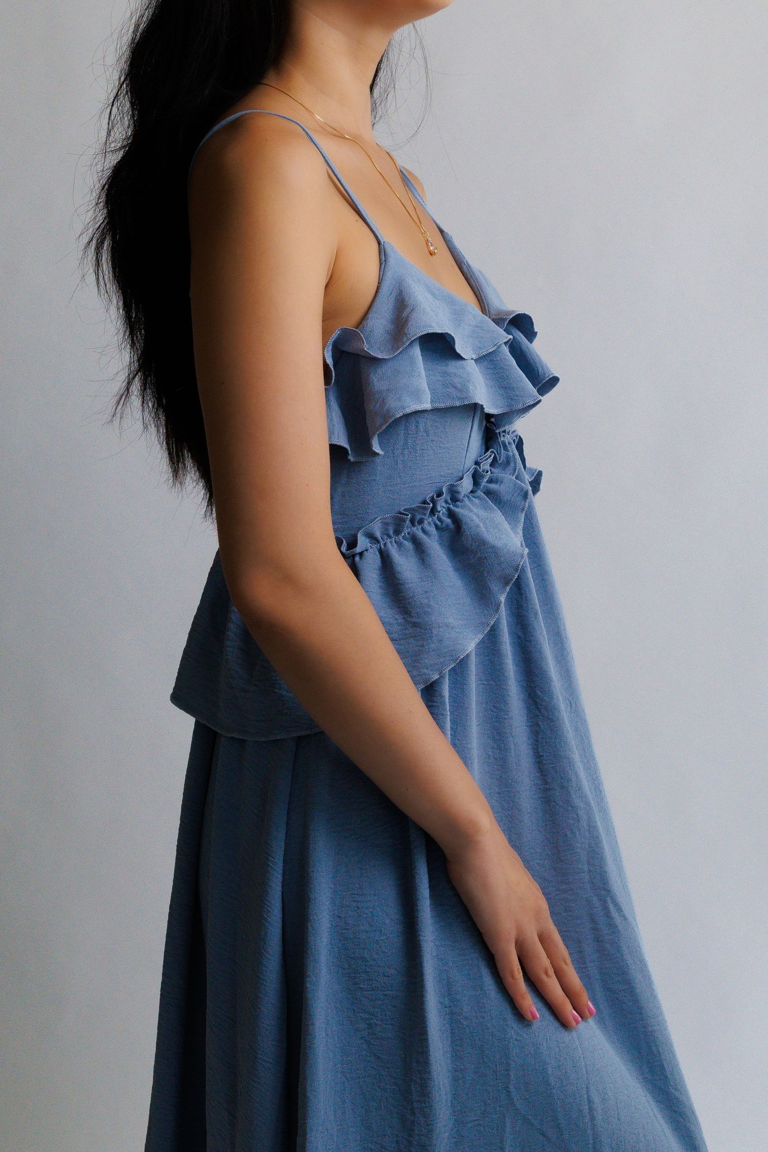 Woman wearing a blue ruffle midi dress with spaghetti straps and tiered frill detail.