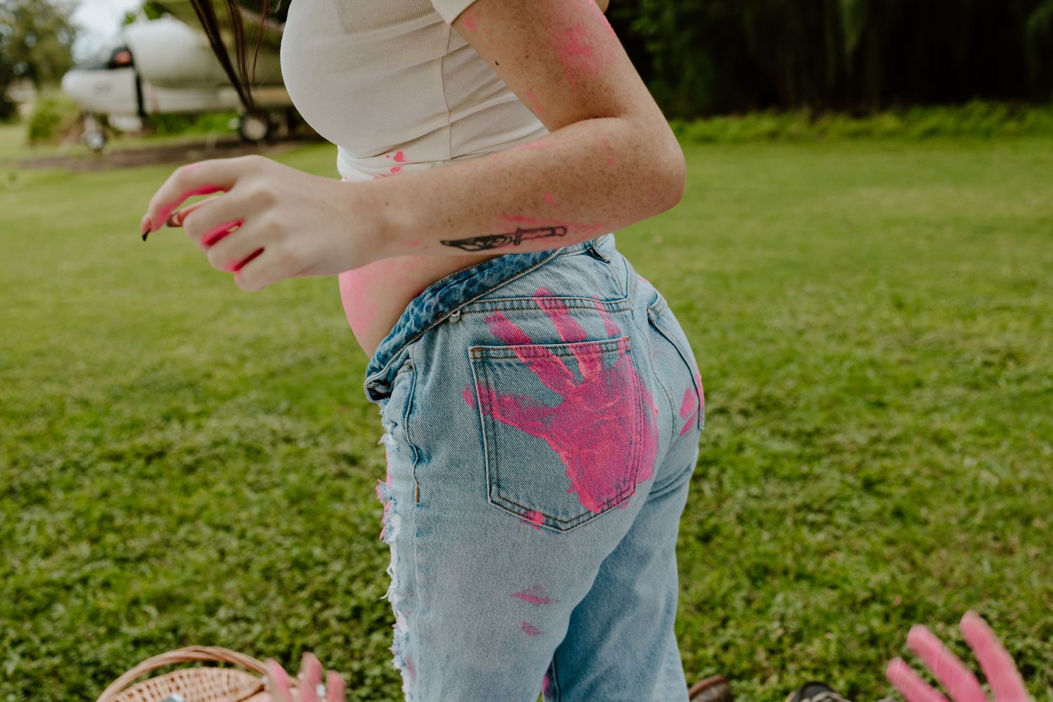 Woman in ripped jeans with pink paint handprints outdoors.