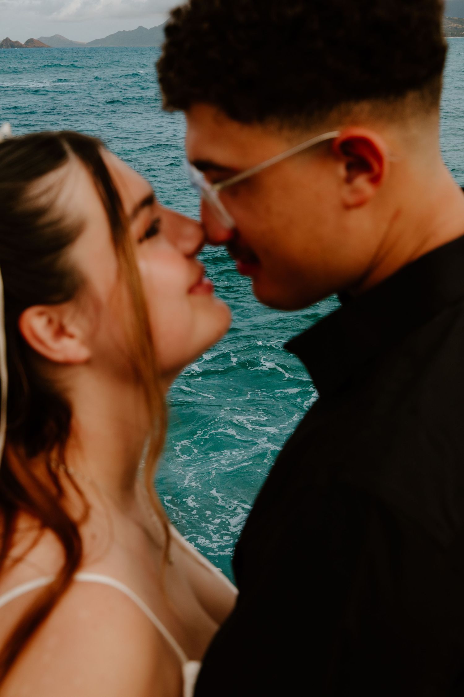 Romantic couple sharing an intimate moment near turquoise ocean waters, with mountains visible in the background.