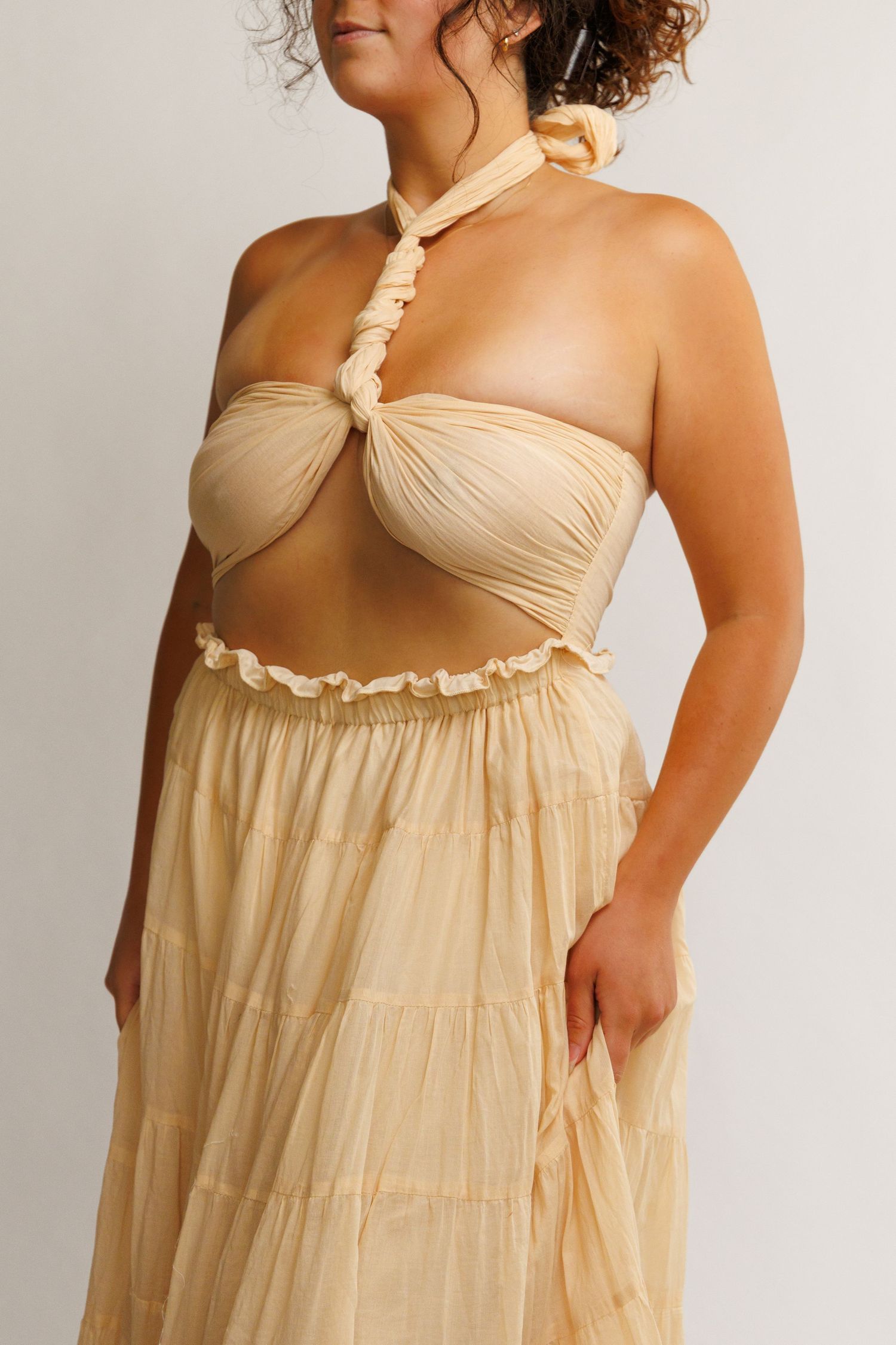 Woman wearing a cream halter crop top with ruched detail and matching tiered maxi skirt set.