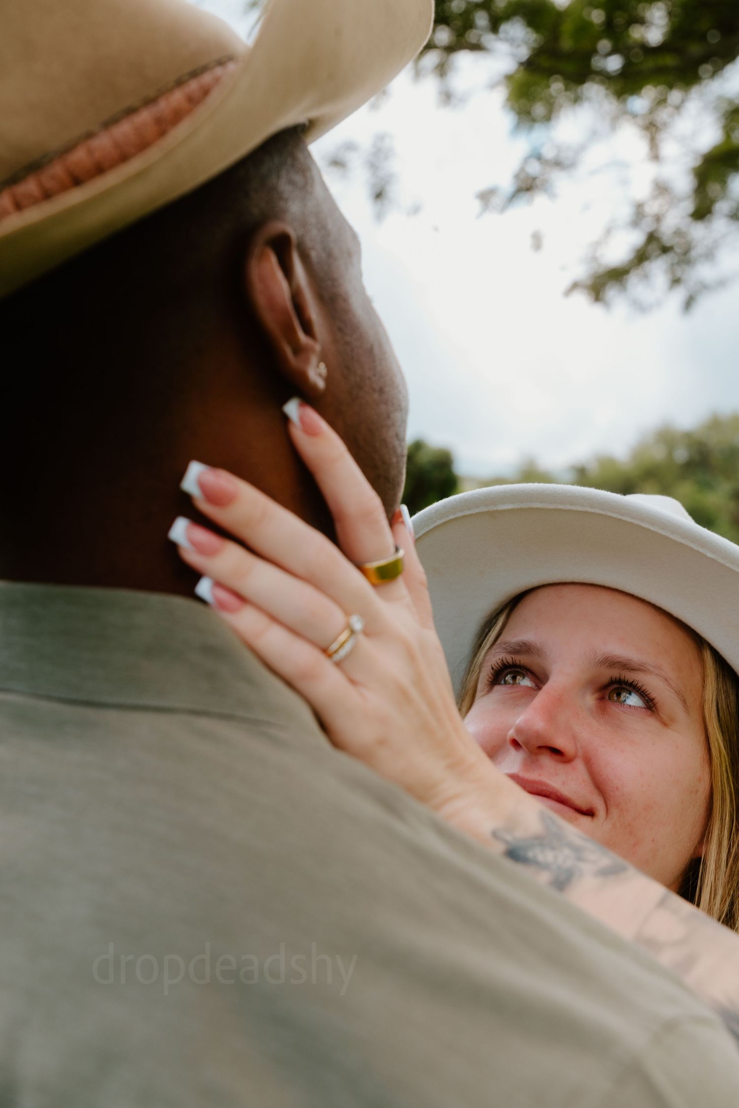 Close-up of interracial couple embracing outdoors, woman with tattooed hand touching mans face.