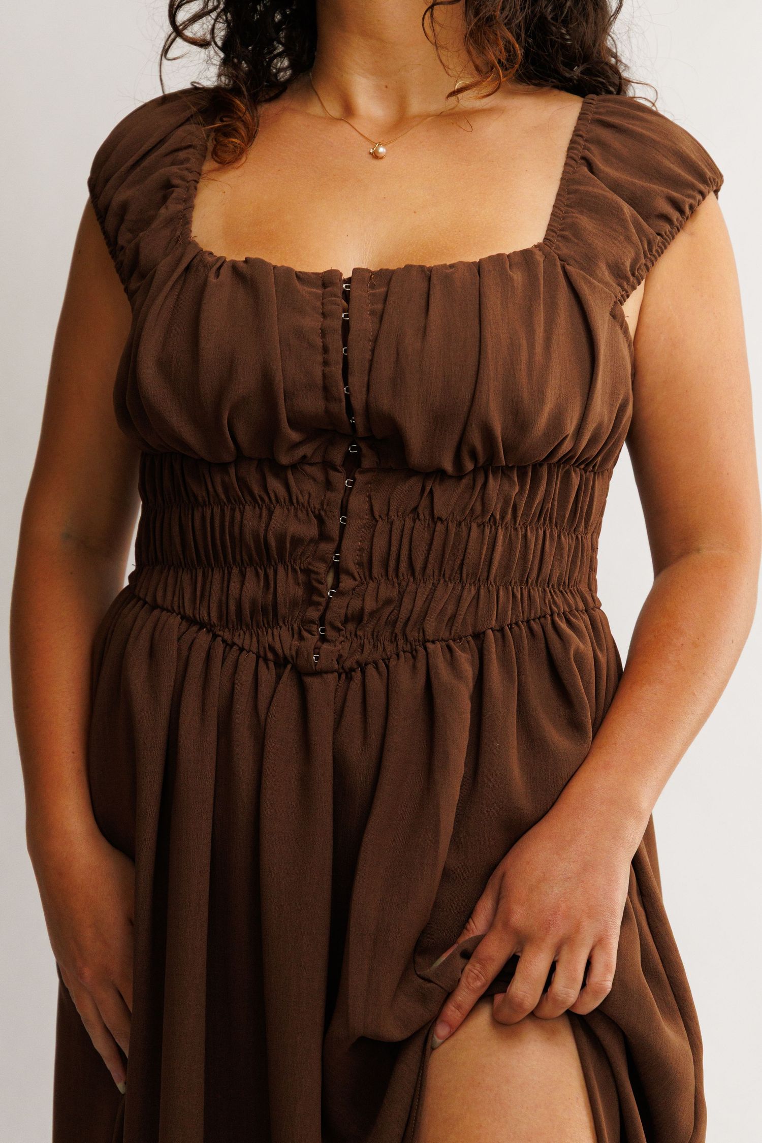 Close-up of a brown smocked corset midi dress with ruffle cap sleeves and button detail on a model.