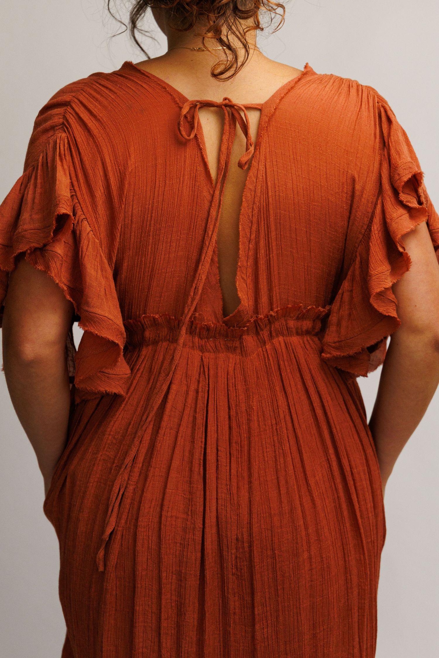 Rust orange maxi dress with flutter sleeves, open tie back detail, and smocked waist, shown from behind.