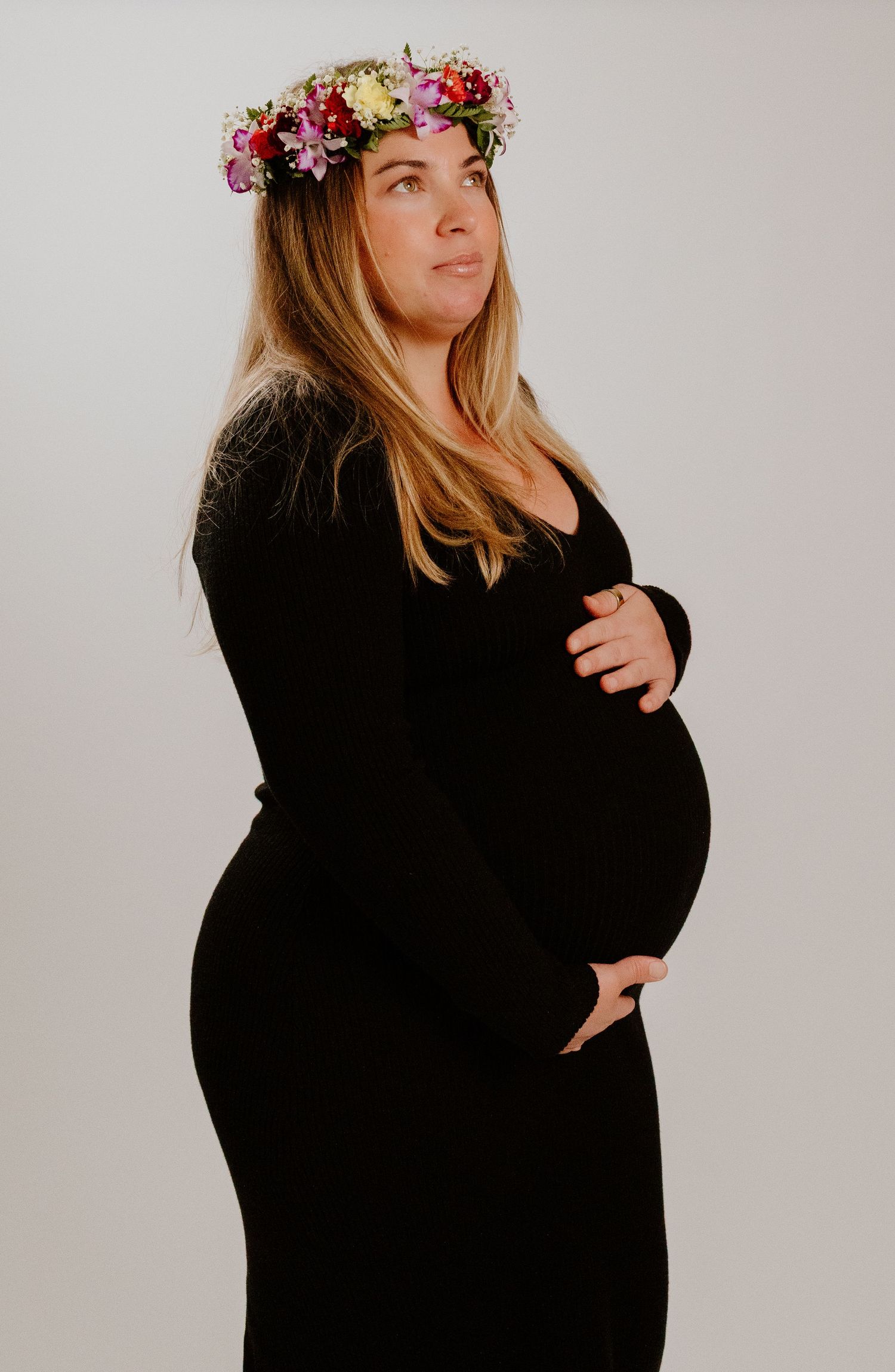 Pregnant woman in black dress with colorful flower crown during studio maternity session.