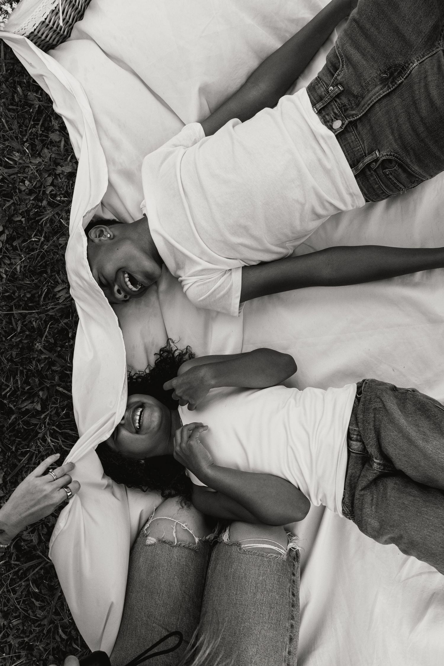 Black and white overhead photo of two kids laughing while lying on a white blanket.