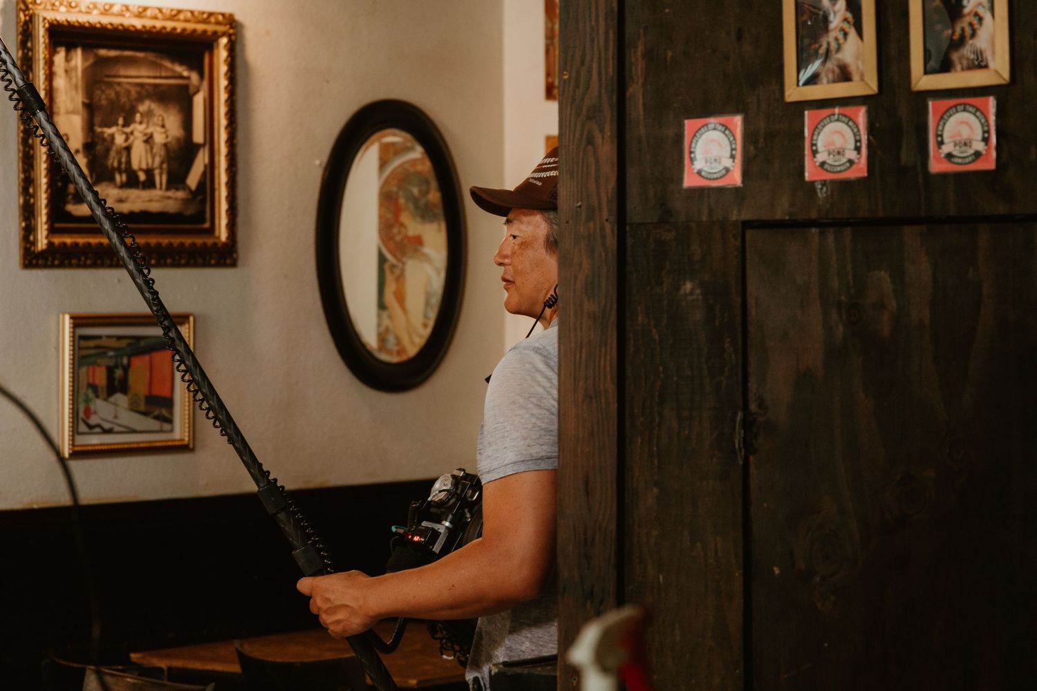 Man in cowboy hat playing guitar in rustic room with vintage framed artwork on walls.