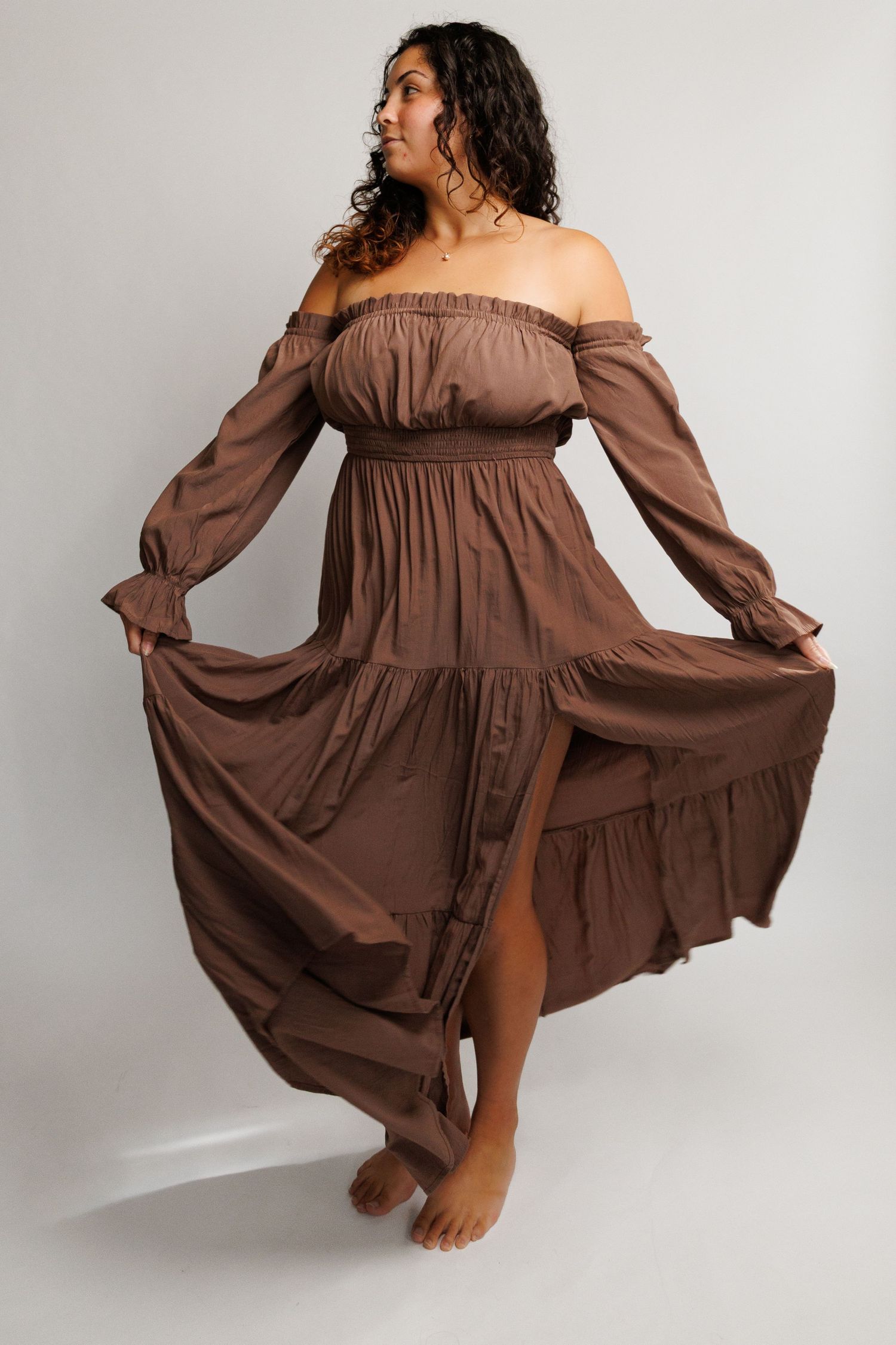 Woman wearing a brown off-shoulder tiered maxi dress with long sleeves and smocked waist, flowing skirt.