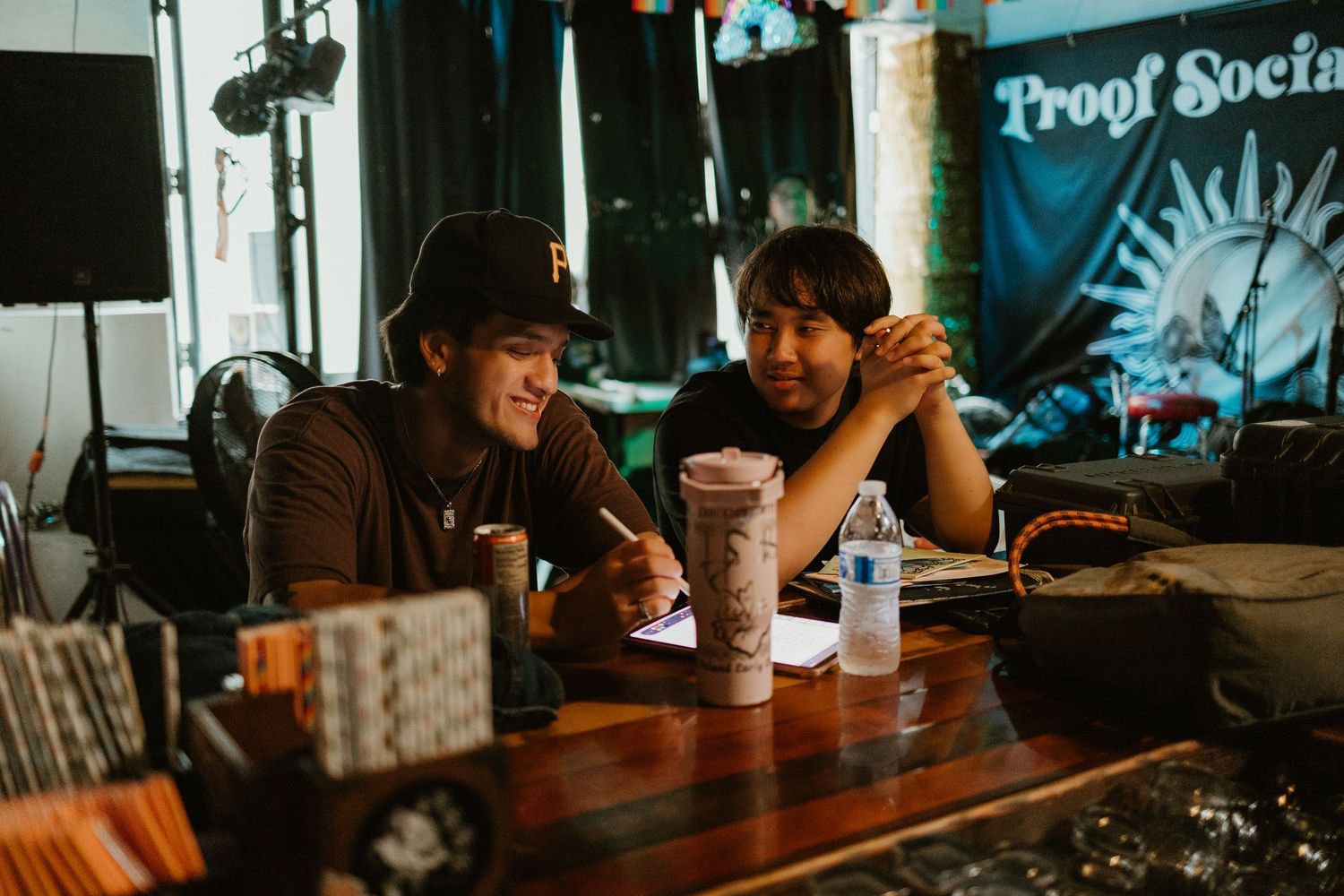 Two men collaborating at a wooden table in a bar with a Proof Society banner behind them.