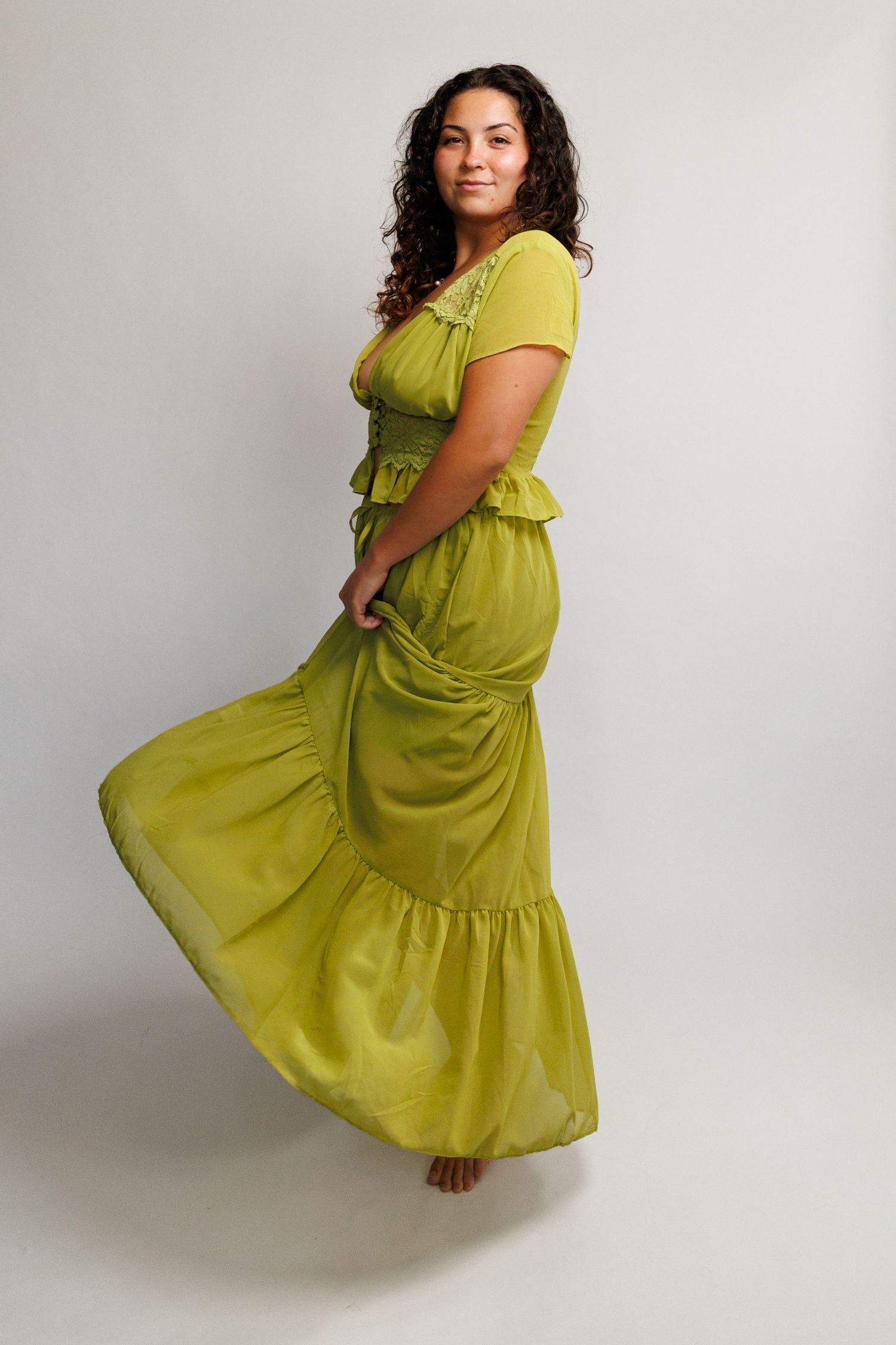 Woman in flowing olive green maxi dress posing gracefully in studio, showcasing tiered skirt and ruched bodice.