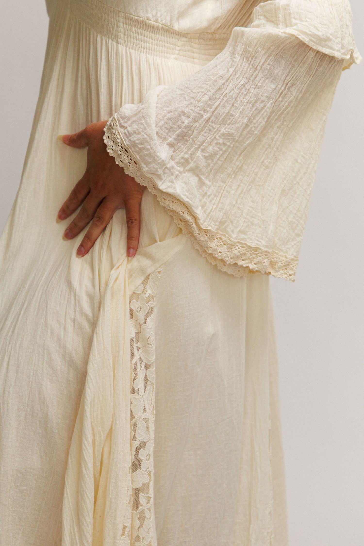 Close-up of a cream lace-trimmed dress with flowing fabric and delicate lace details on sleeves and hem.