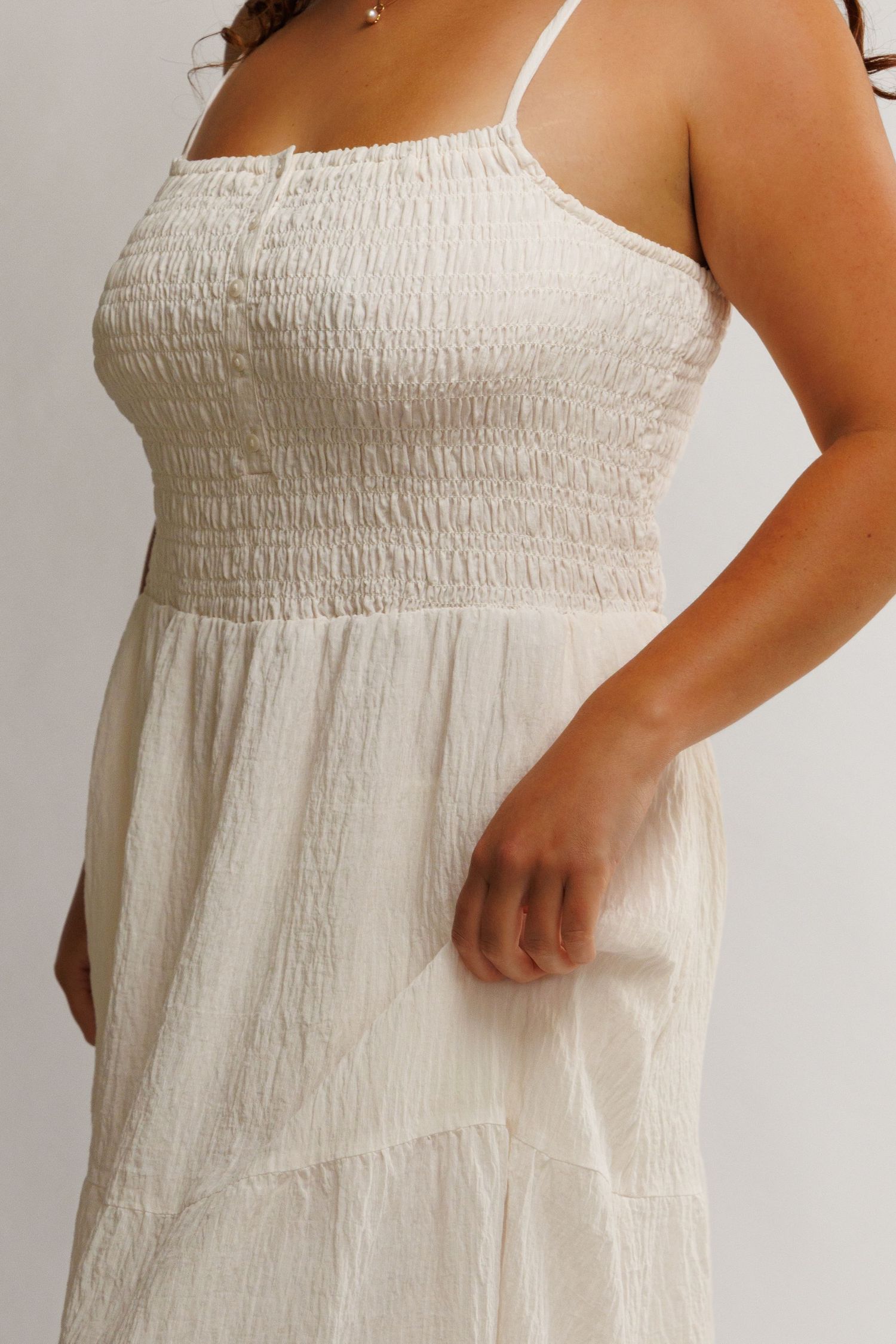 Woman wearing a white smocked bodice spaghetti strap midi dress with tiered skirt in textured fabric.