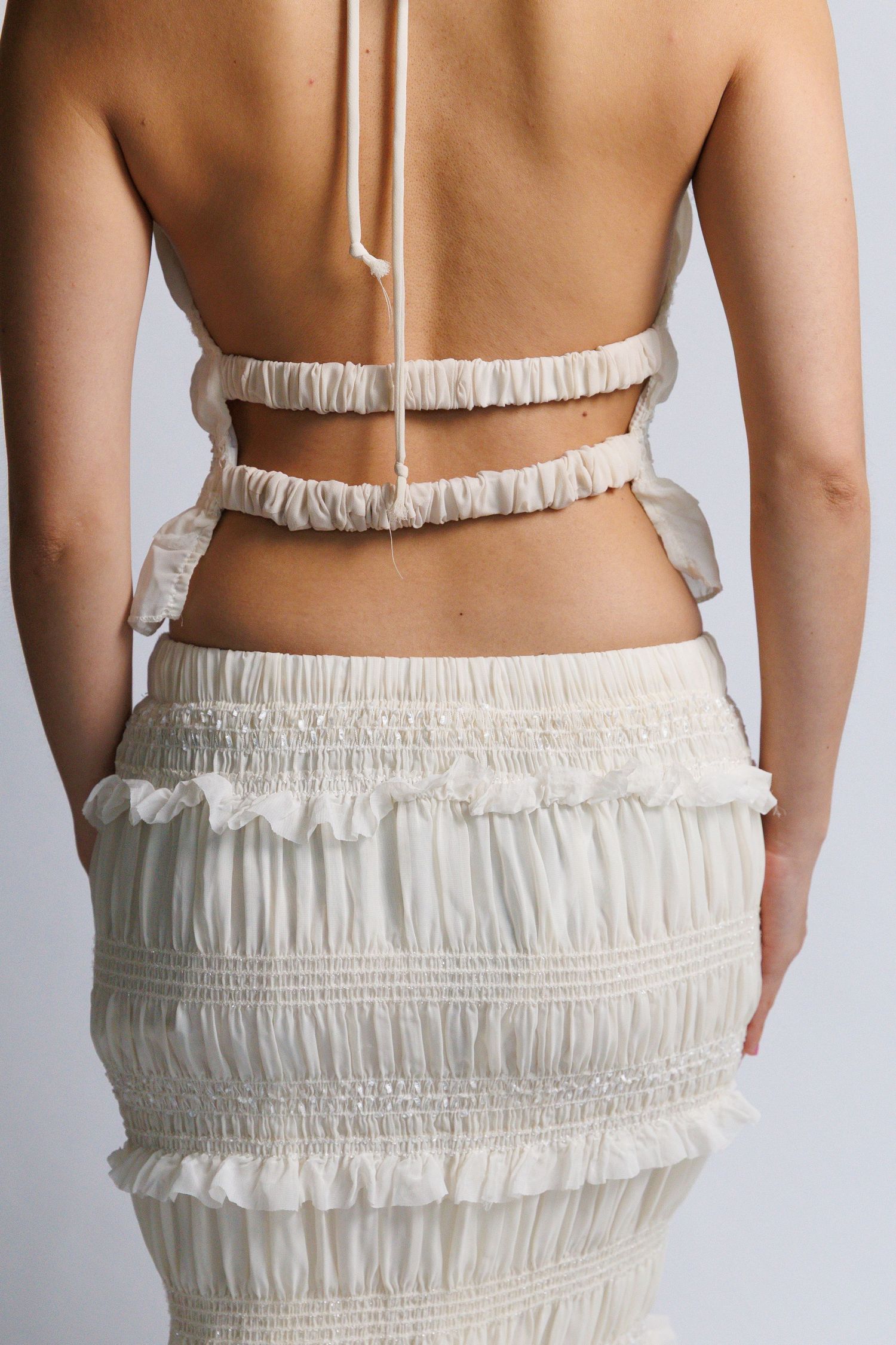 Woman wearing a white ruffled crop top and matching smocked midi skirt, shown from the back.
