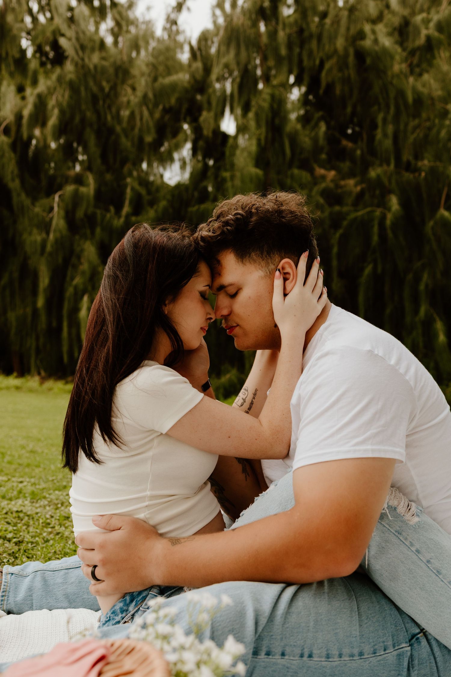 Couple tenderly embracing face to face while sitting on a blanket in a green outdoor setting.