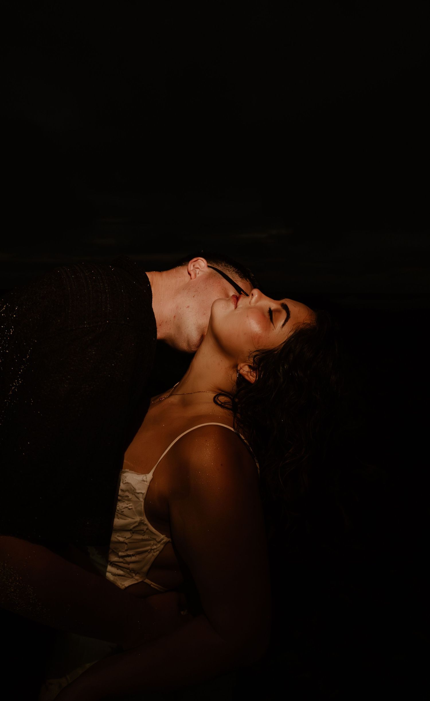 A woman in a white dress tilts her head back with eyes closed in dramatic low-key lighting.