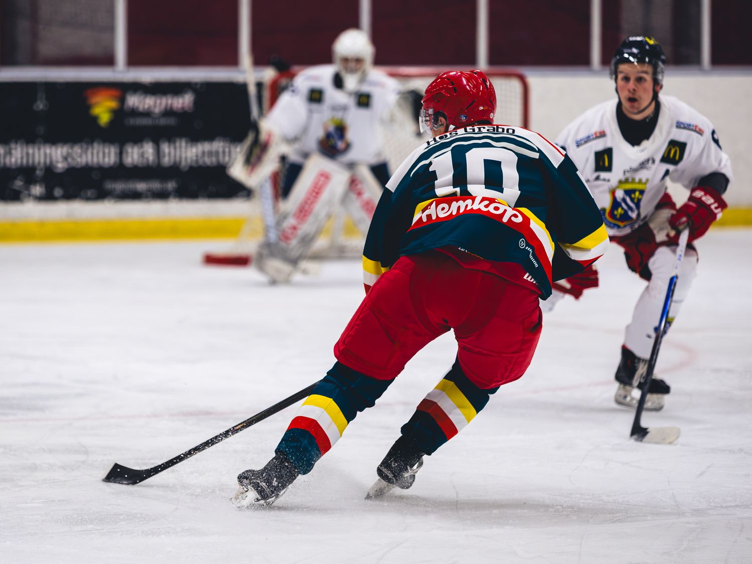 Ice hockey players in red and dark uniforms chase after the puck during an intense match.