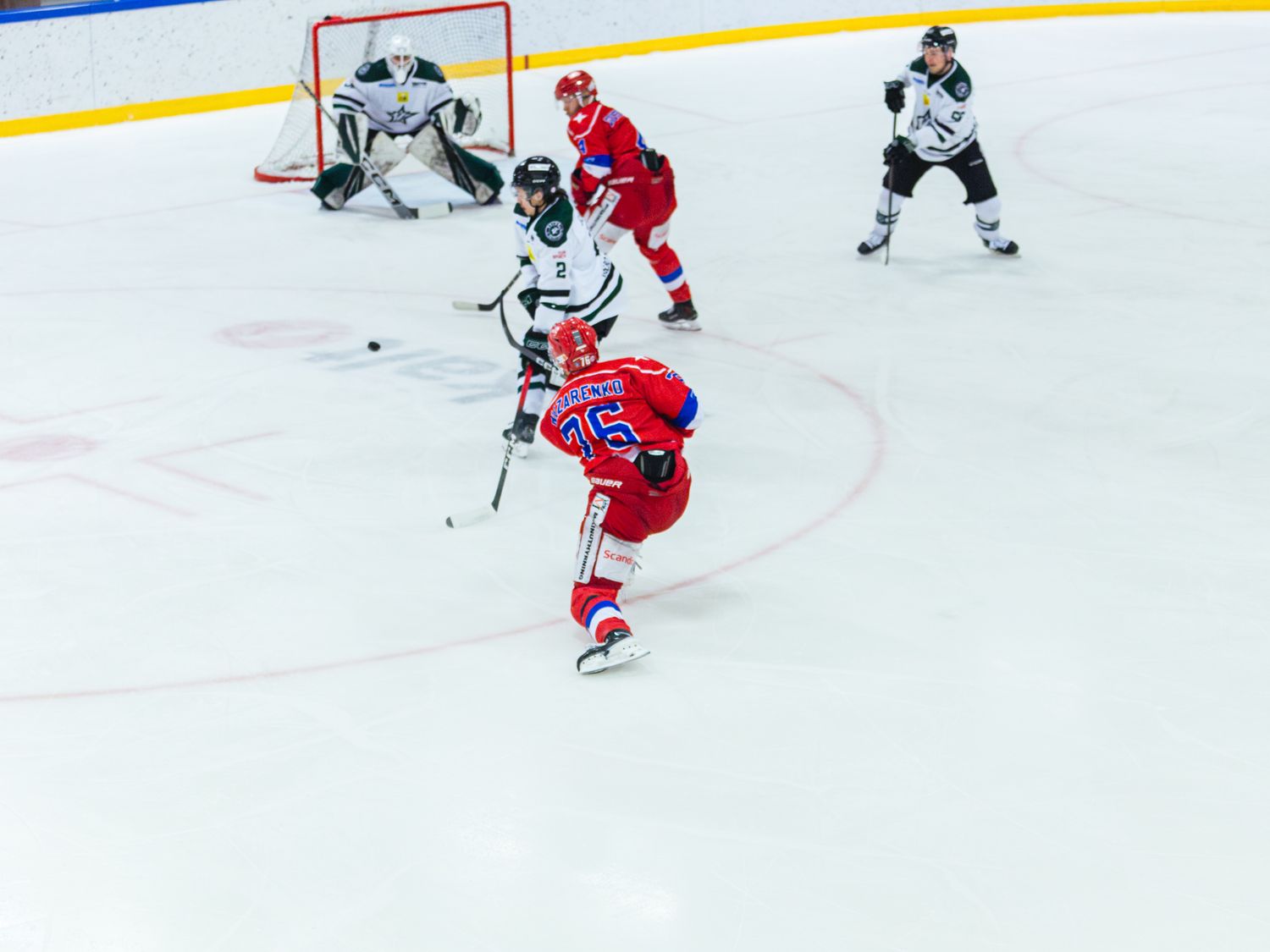 Wide shot of a hockey game showing players near the goal net with red and white uniforms.