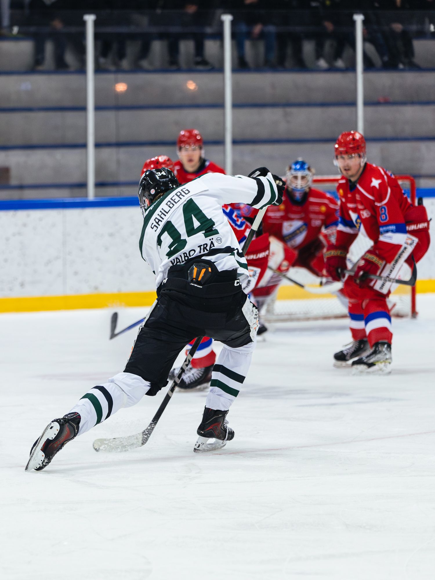 Hockey players in black and red uniforms battle for position on the ice.