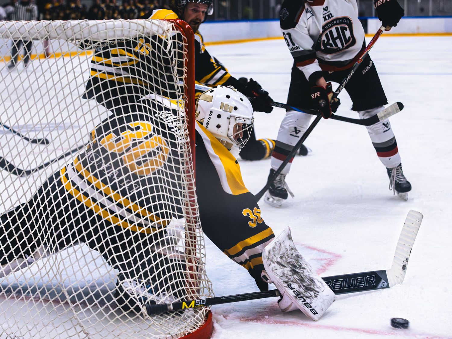 Hockey goalie in yellow defends against attacking players near the crease.