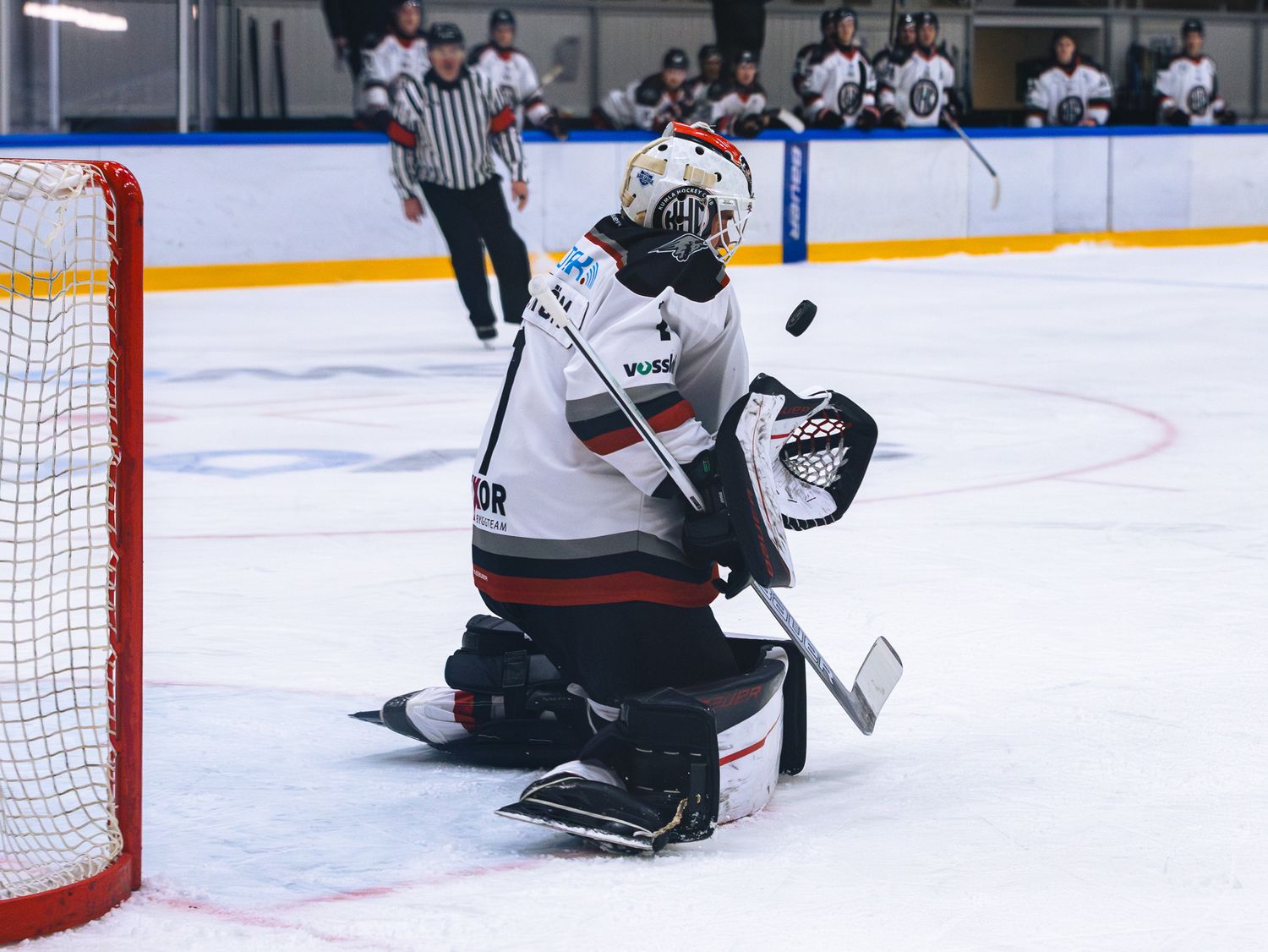 A goalie makes a dramatic save in front of the hockey net.