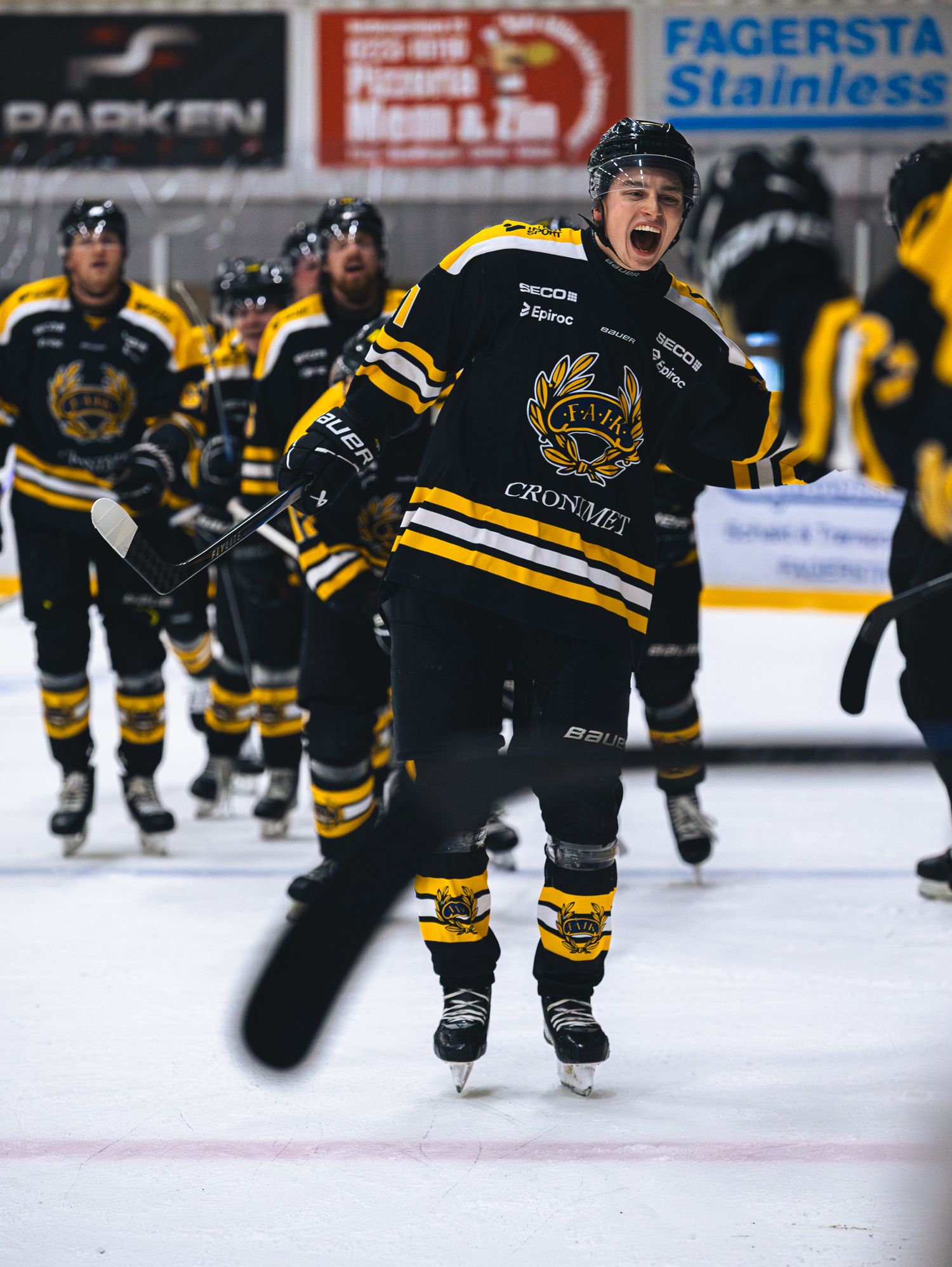 Youth hockey players in black and gold uniforms celebrating on the ice.