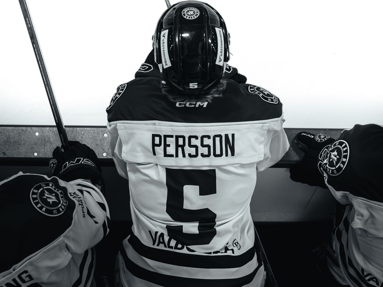 Hockey players in black and white jerseys line up along the boards during a game.