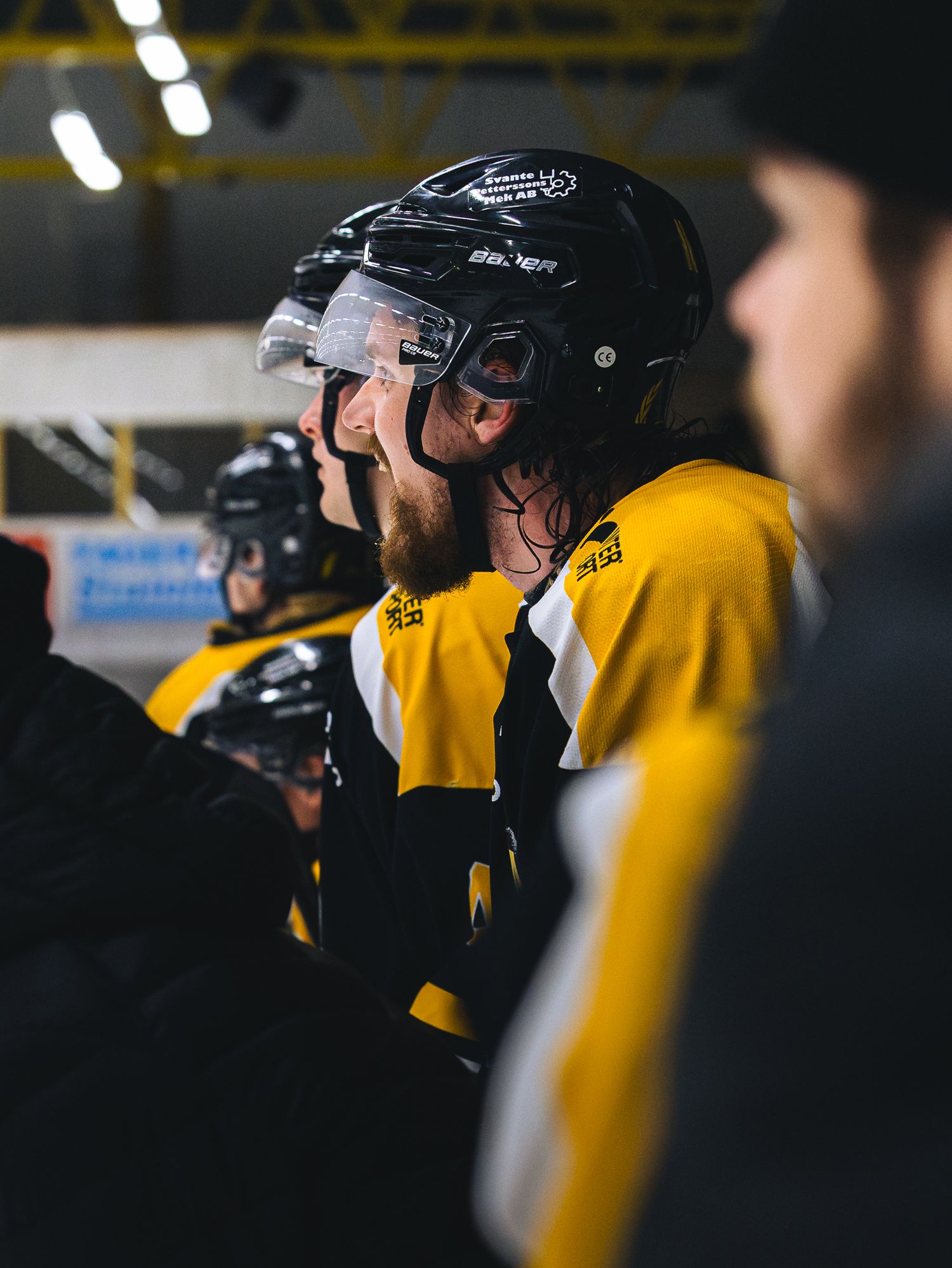 Hockey players in yellow and black jerseys watching from the bench during game.