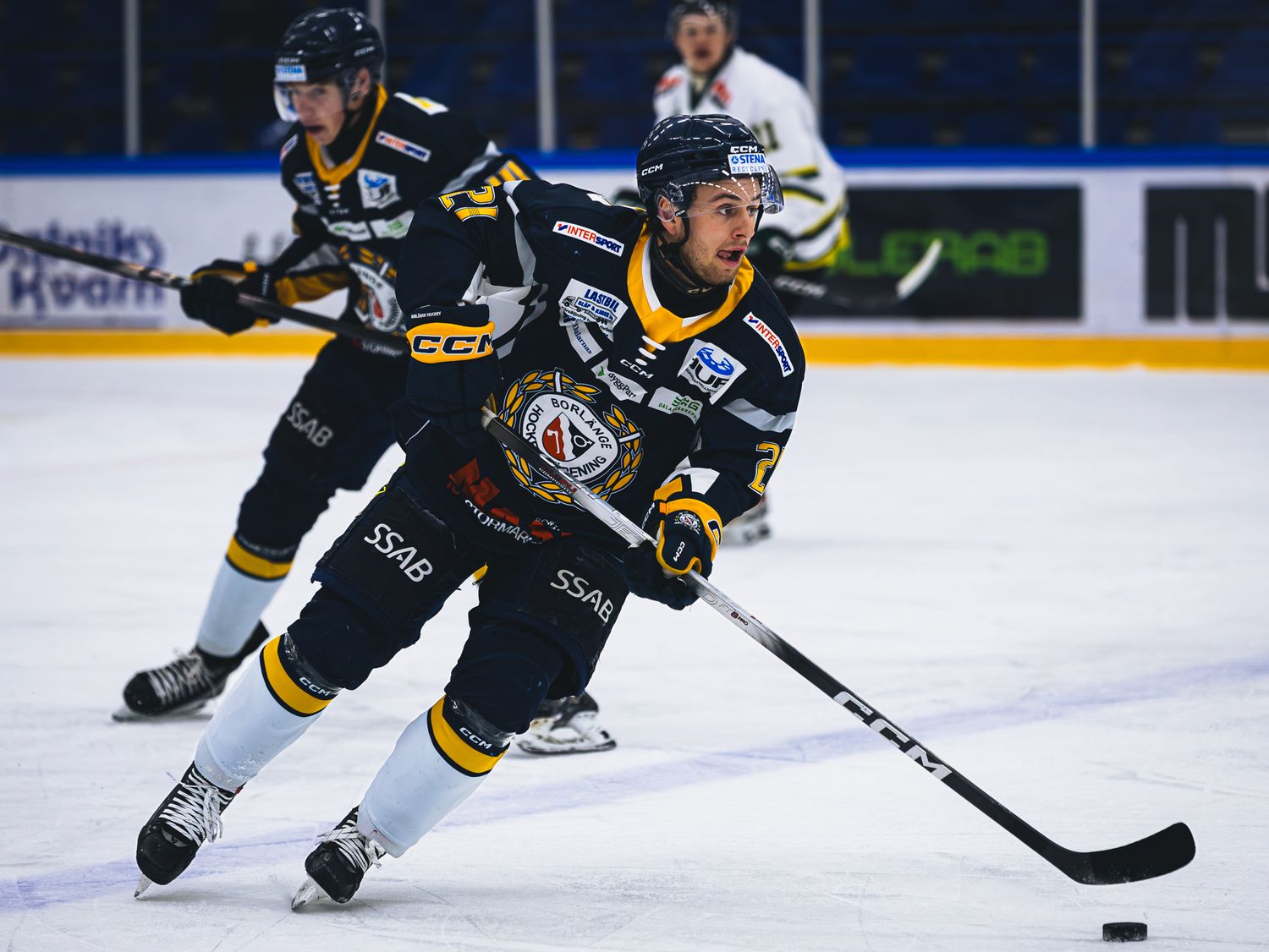 Hockey player in black and yellow uniform skates with puck on ice during competitive match.