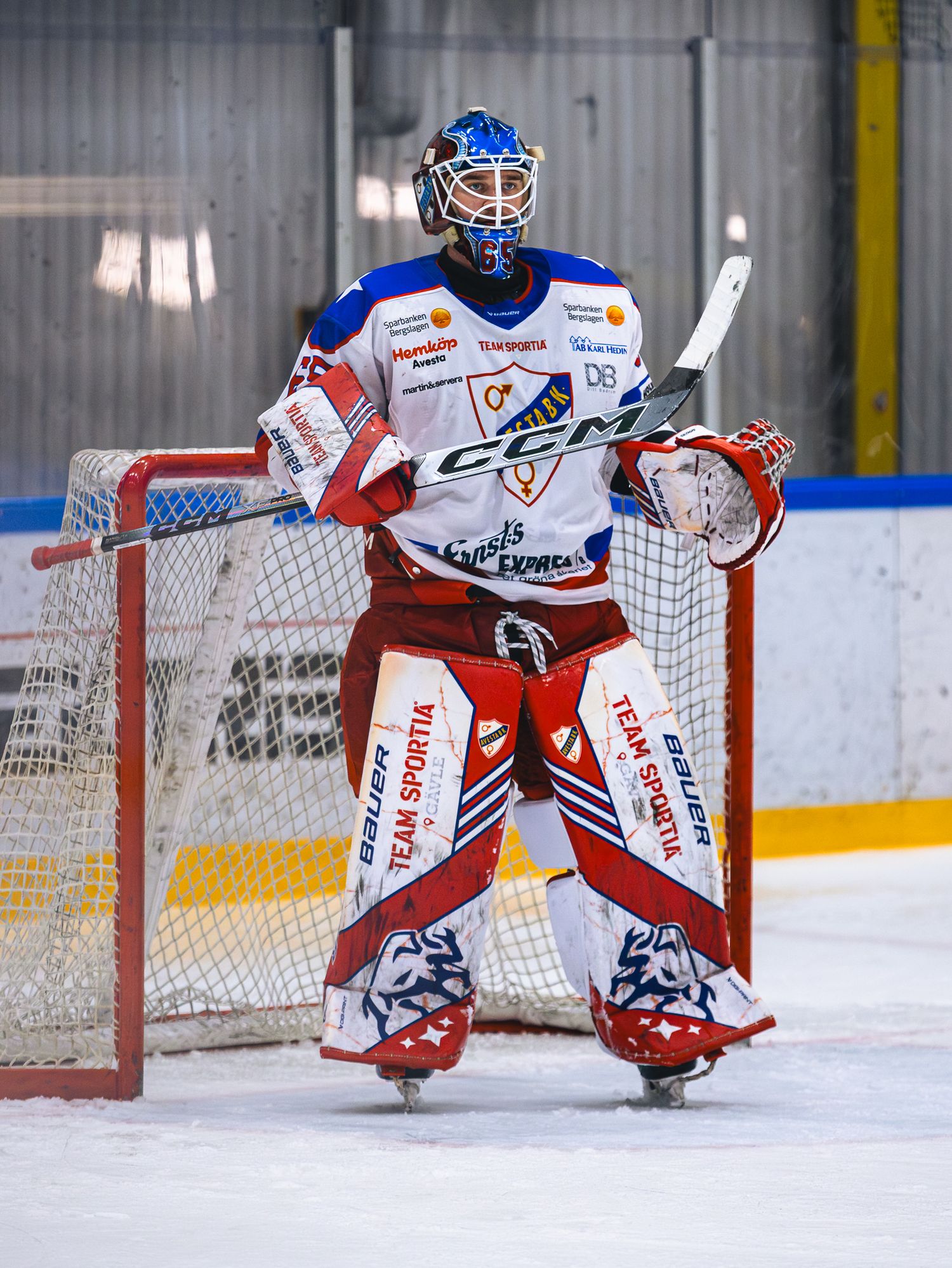 Hockey goalie in blue and white uniform crouches in ready position at the net.