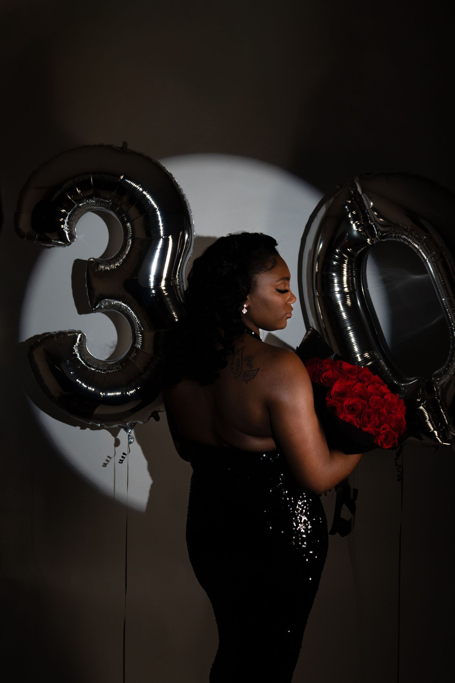 Glamorous portrait with black number 30 balloons and red roses in dramatic lighting.