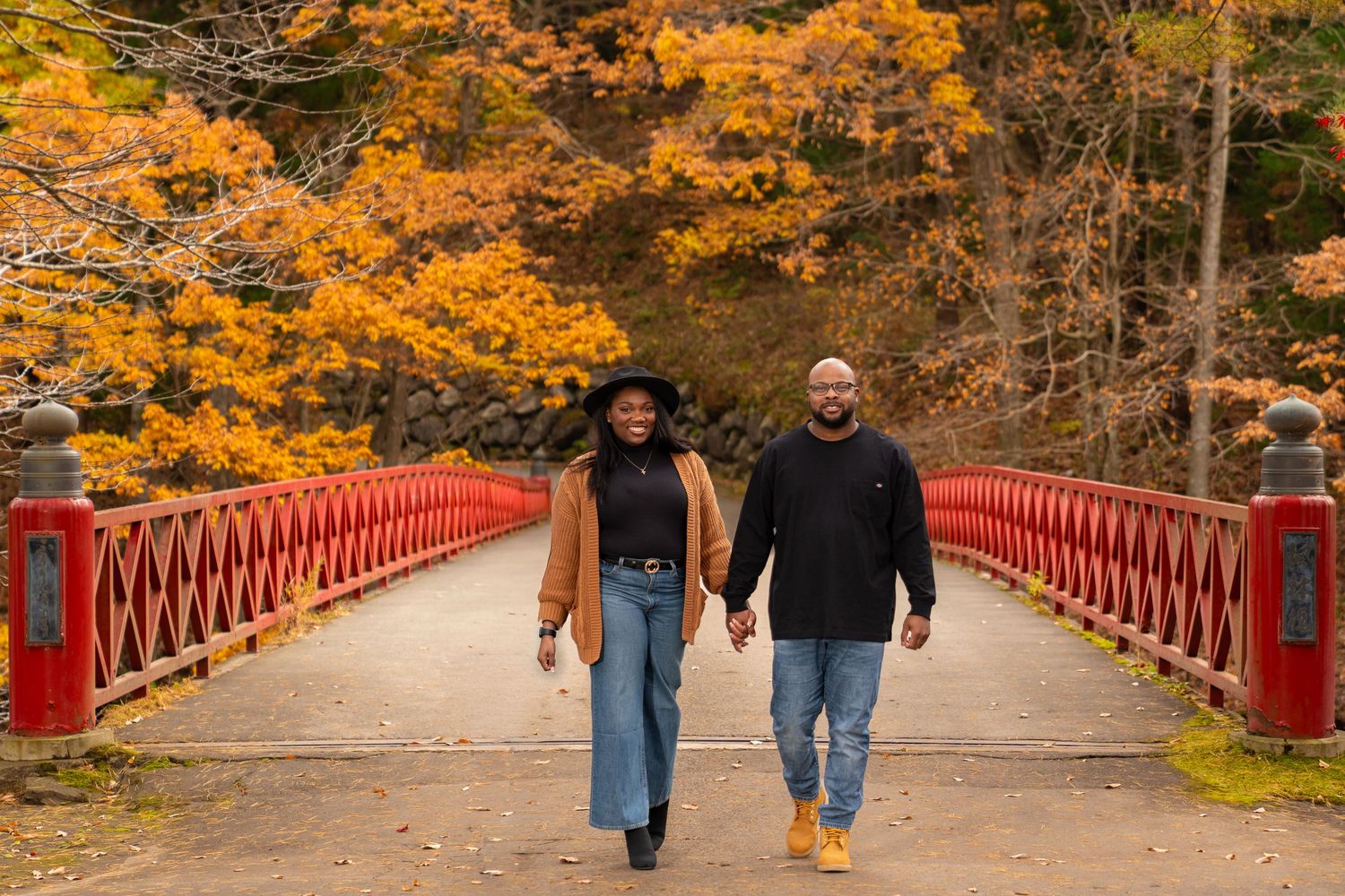 Red bridge walkway surrounded by golden autumn trees and fallen leaves.
