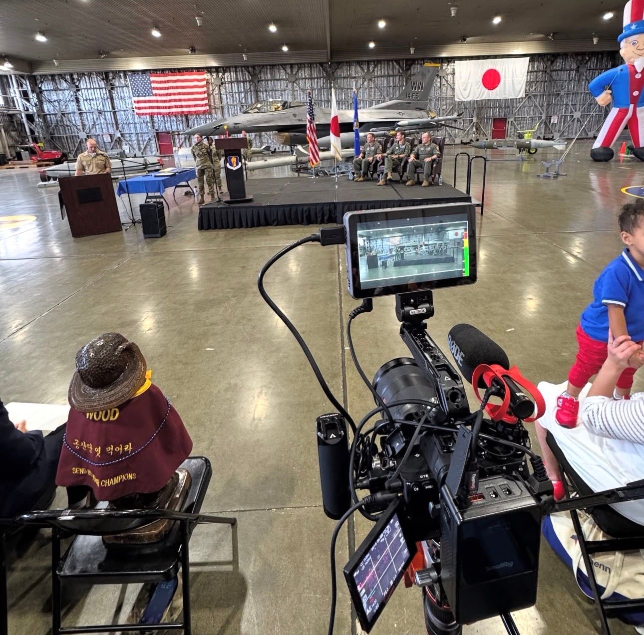 Professional video camera setup in venue with American and Japanese flags displayed.