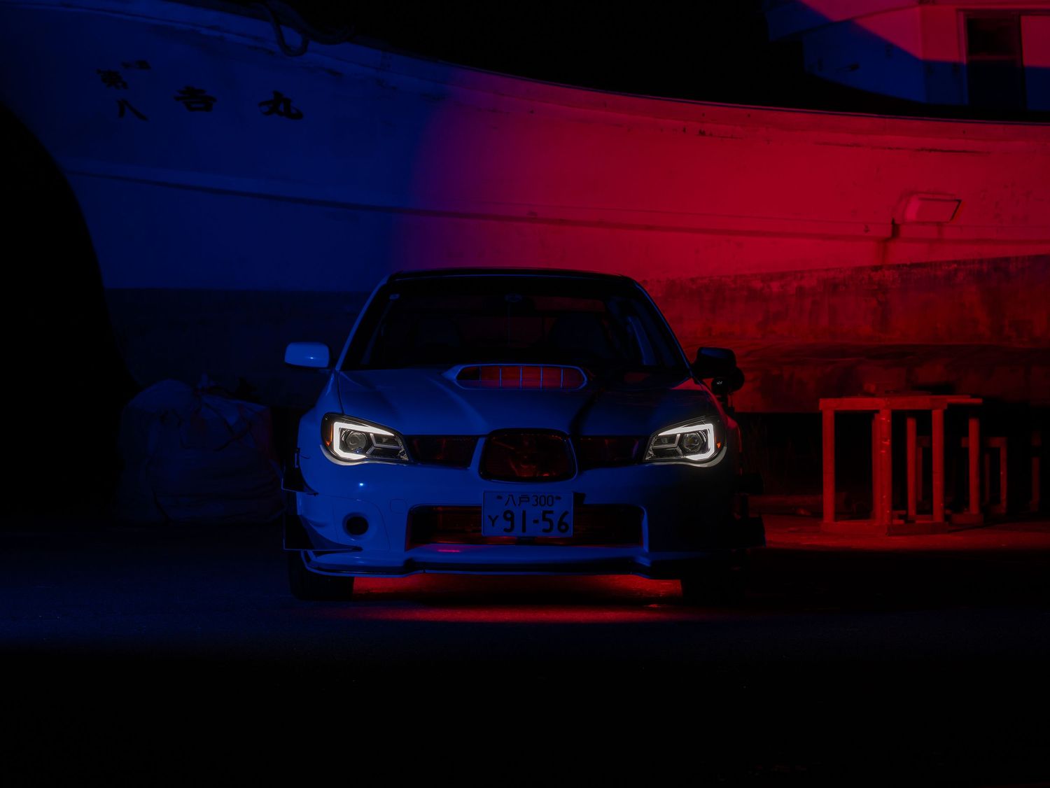 BMW M4 sports car with glowing headlights photographed at night in dramatic red and blue lighting.