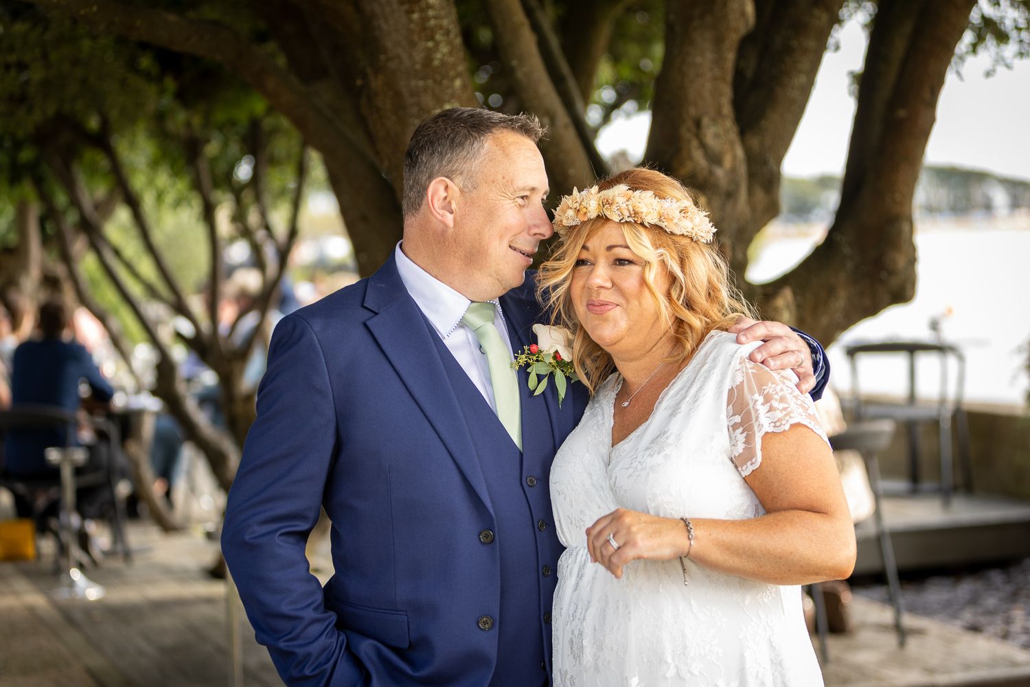 A couple shares romantic moments in formal wedding attire against an outdoor backdrop.